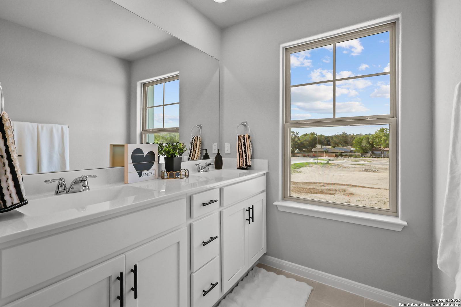 Modern double vanity bathroom with white cabinets, large window view, and plants in Davidson Homes Gillian C, San Antonio