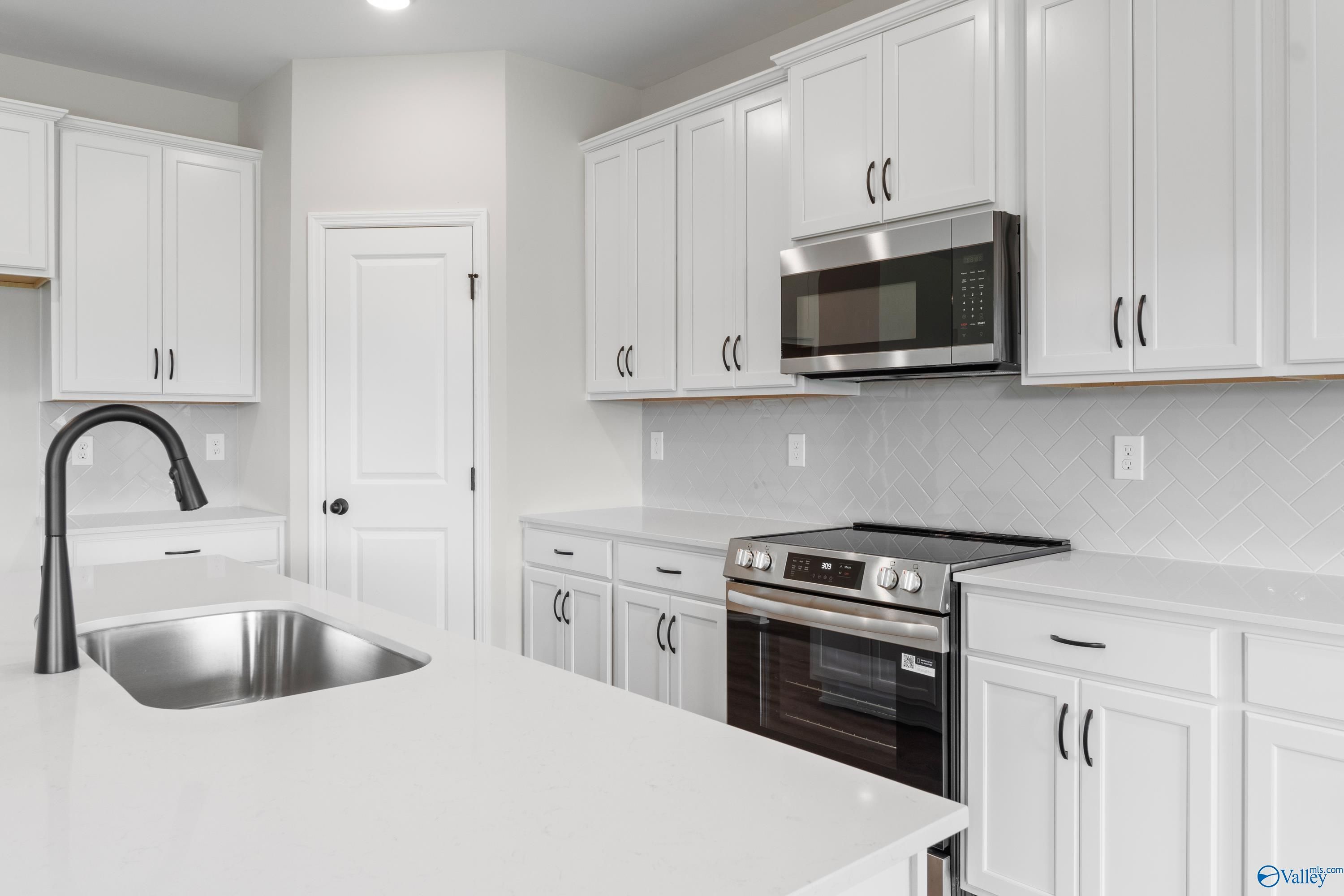 Modern white kitchen with stainless appliances, quartz counters, and subway tile backsplash in Davidson Homes The Rockford, Toney, AL