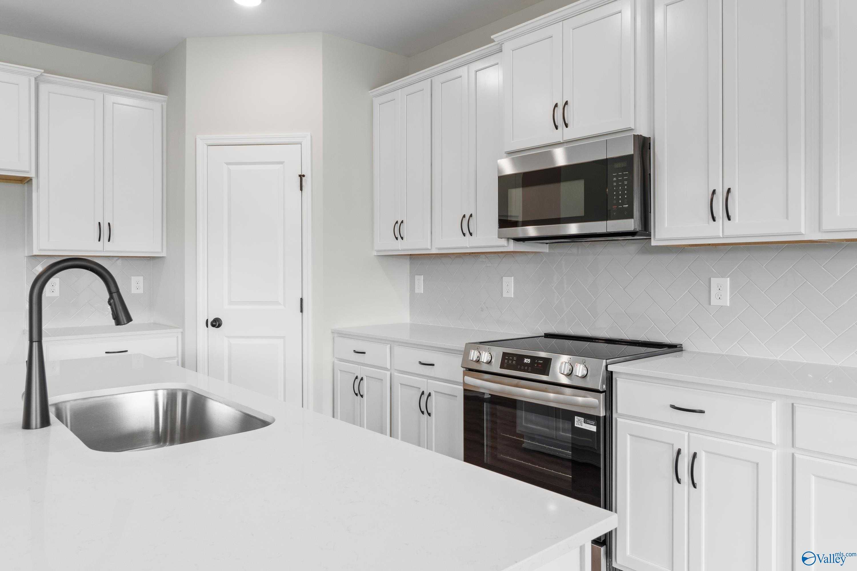 Modern white kitchen with stainless appliances, quartz counters, and subway tile backsplash in Davidson Homes The Rockford, Toney, AL
