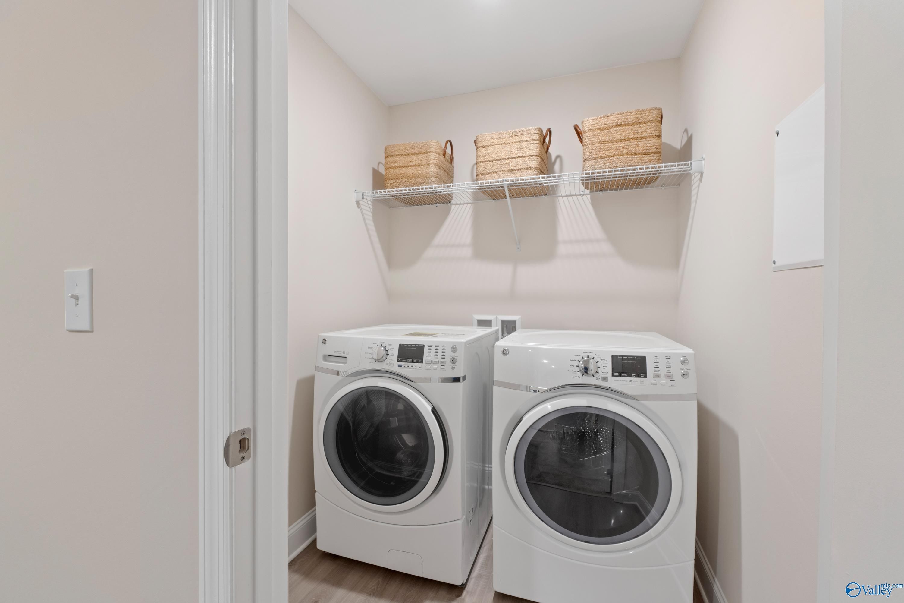 Functional laundry room with side-by-side white washers, dryers, and wicker basket shelves in The Camden floor plan, Huntsville, Alabama