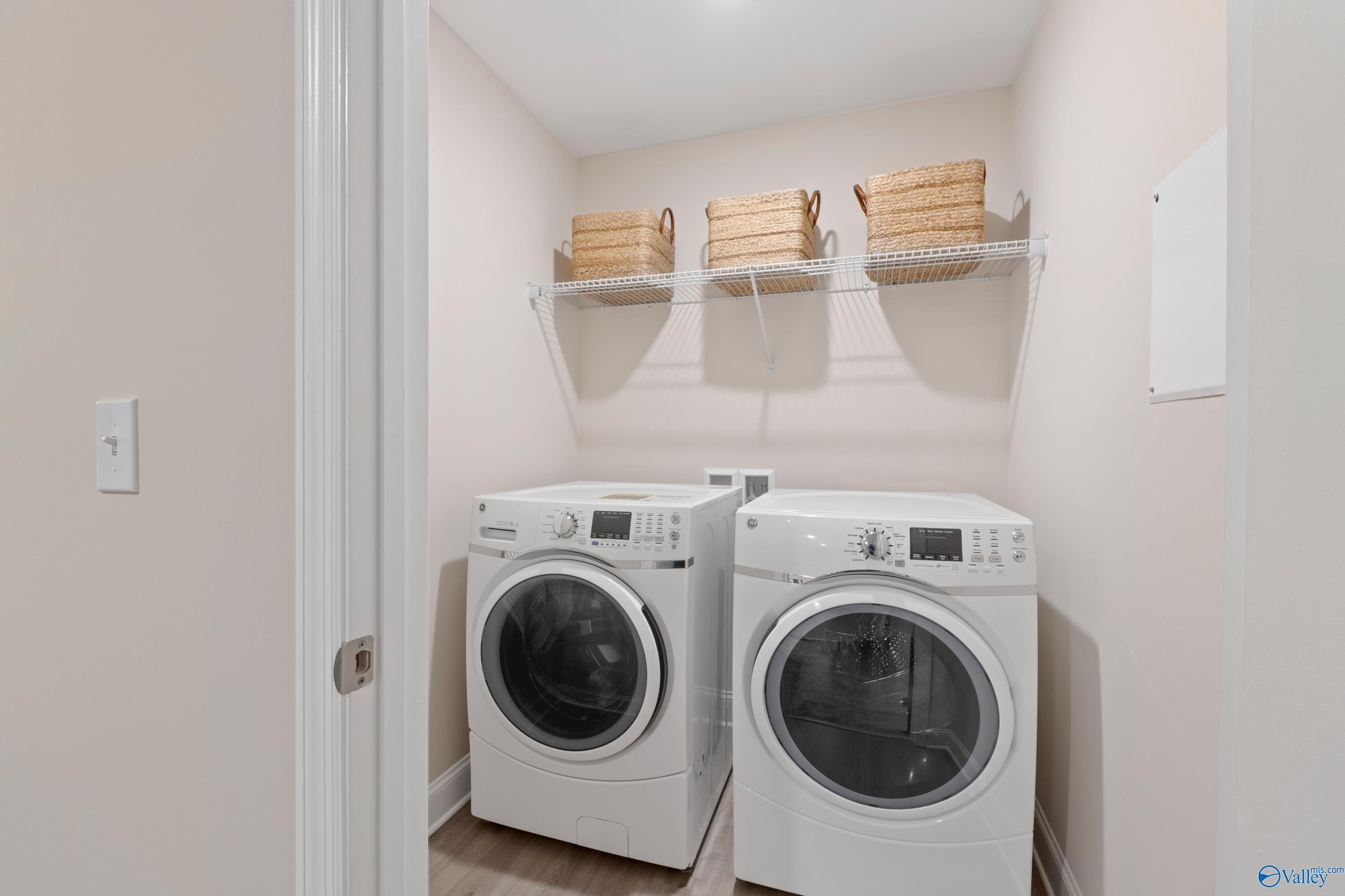 Functional laundry room with side-by-side white washers, dryers, and wicker basket shelves in The Camden floor plan, Huntsville, Alabama
