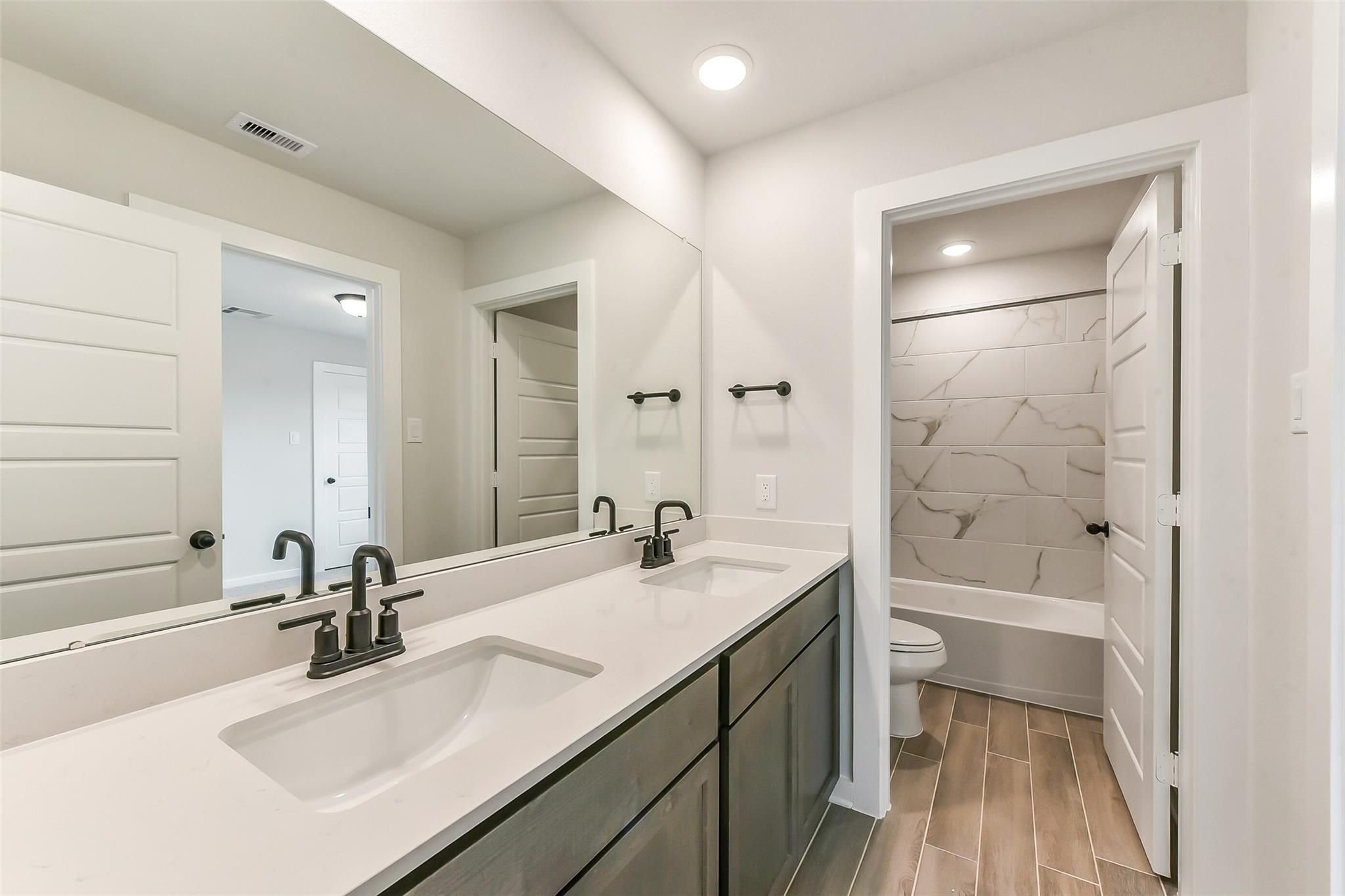 Modern master bathroom featuring double vanity with quartz counters, black faucets, and tiled soaking tub in Davidson Homes Sequoia C, Crosby, Texas