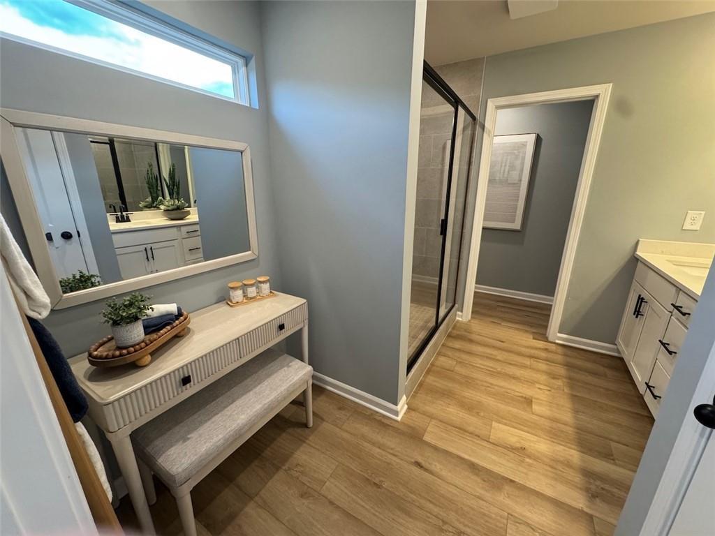 Serene master bathroom with light blue walls, white vanity, glass shower, and wood-look floors in Davidson Homes The Hartwell A, Canton, GA