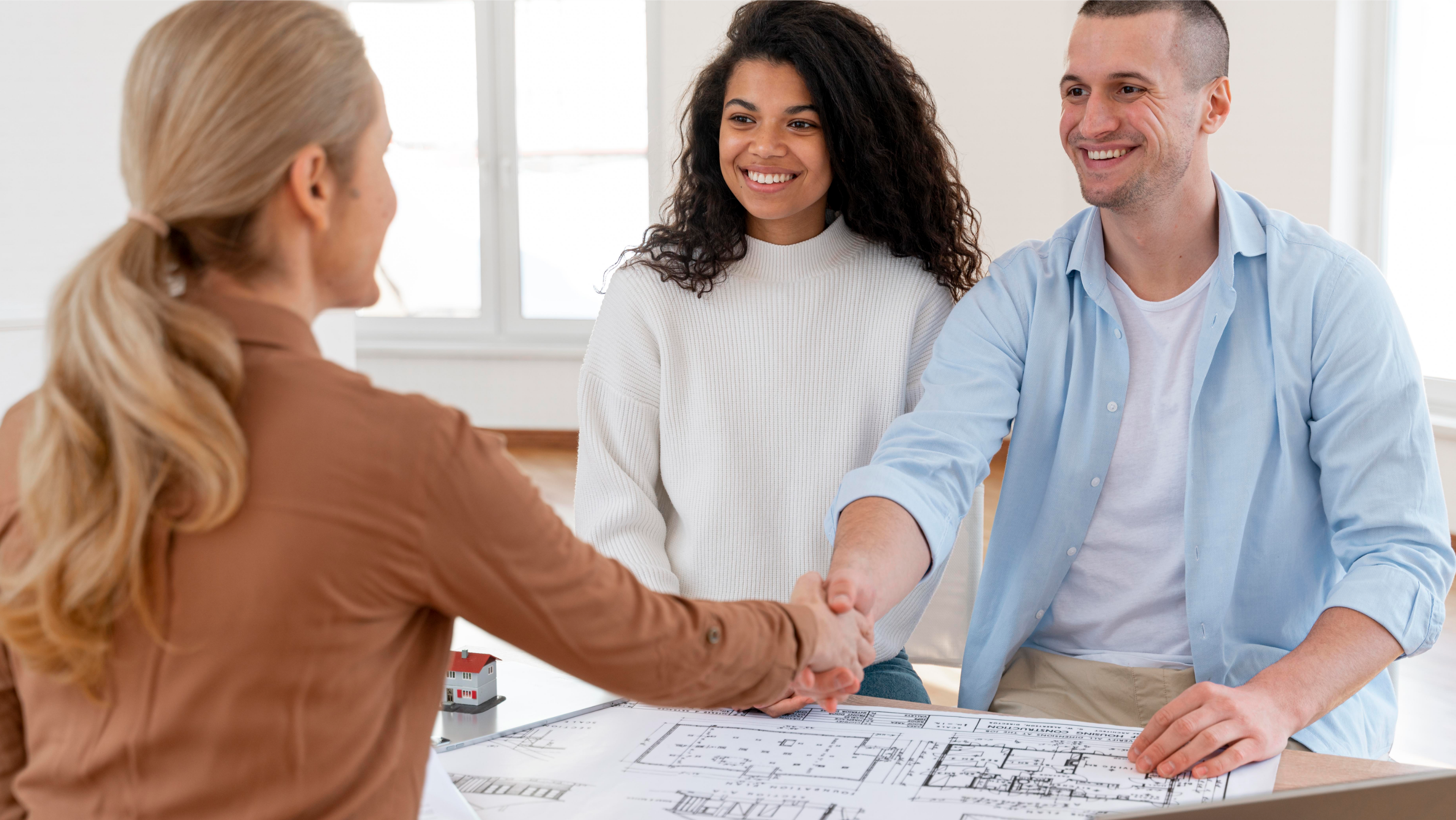Real estate agent shaking hands with smiling couple over blueprints and model home at Davidson Homes seminar