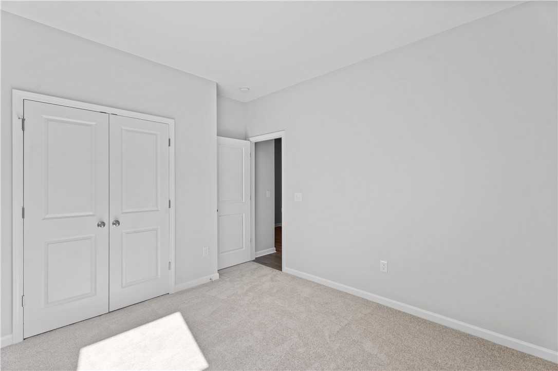 Bright bedroom with white double closet doors and adjacent bath entry on beige carpet in Davidson Homes The Luna B, Opelika, AL
