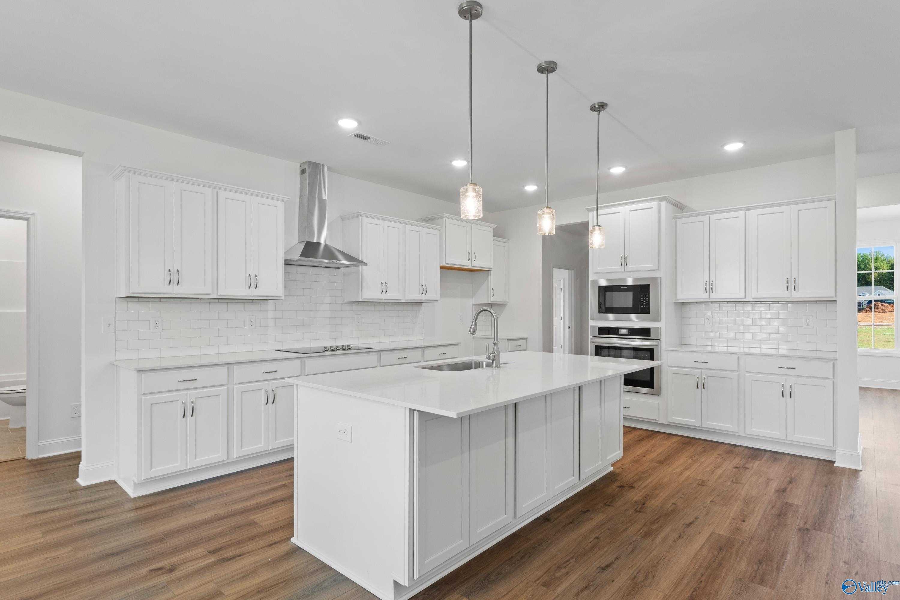 Modern white kitchen featuring large island, stainless steel appliances, subway tile backsplash in Davidson Homes The Oxford, Harvest AL