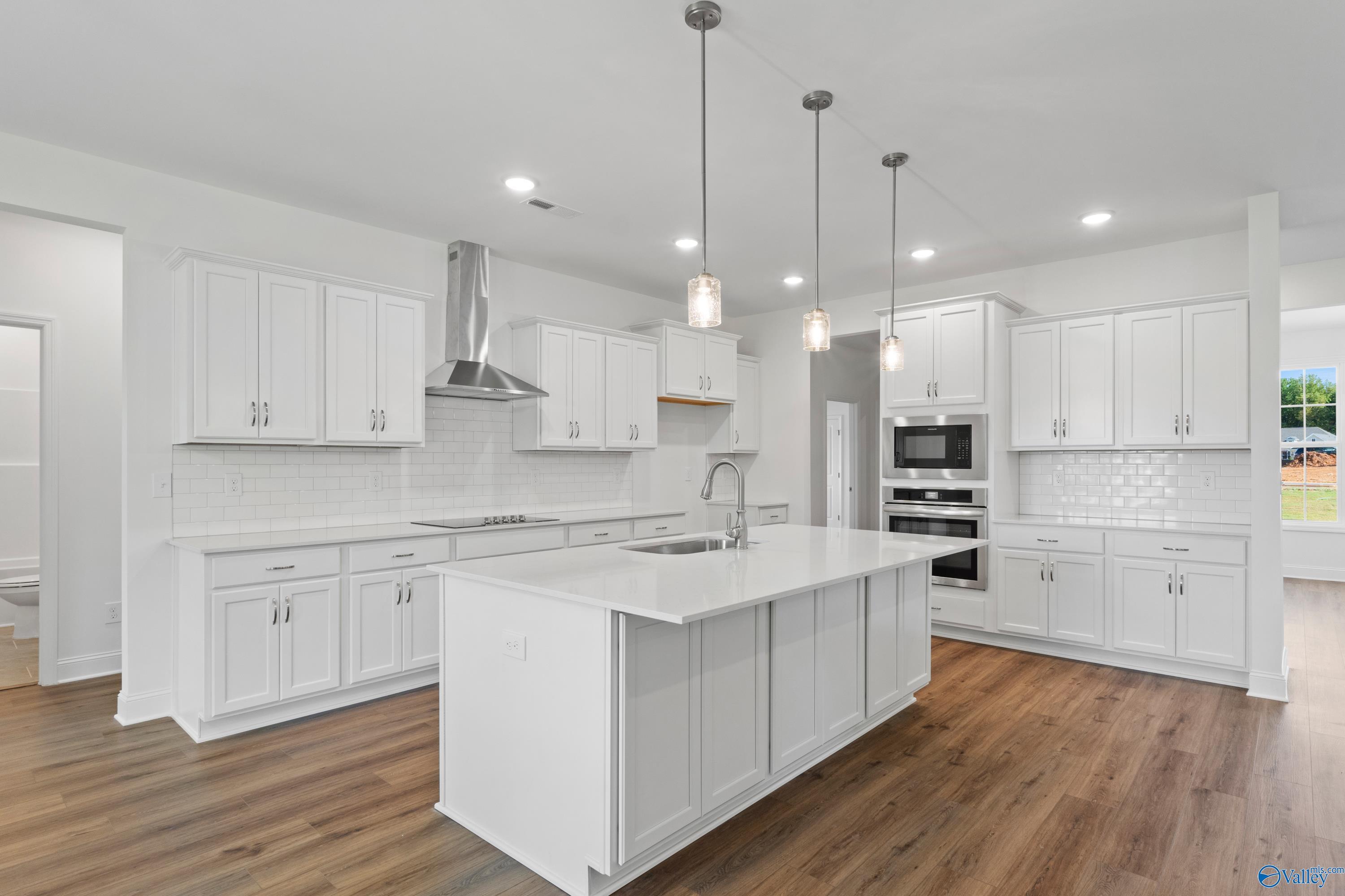 Modern white kitchen featuring large island, stainless steel appliances, subway tile backsplash in Davidson Homes The Oxford, Harvest AL