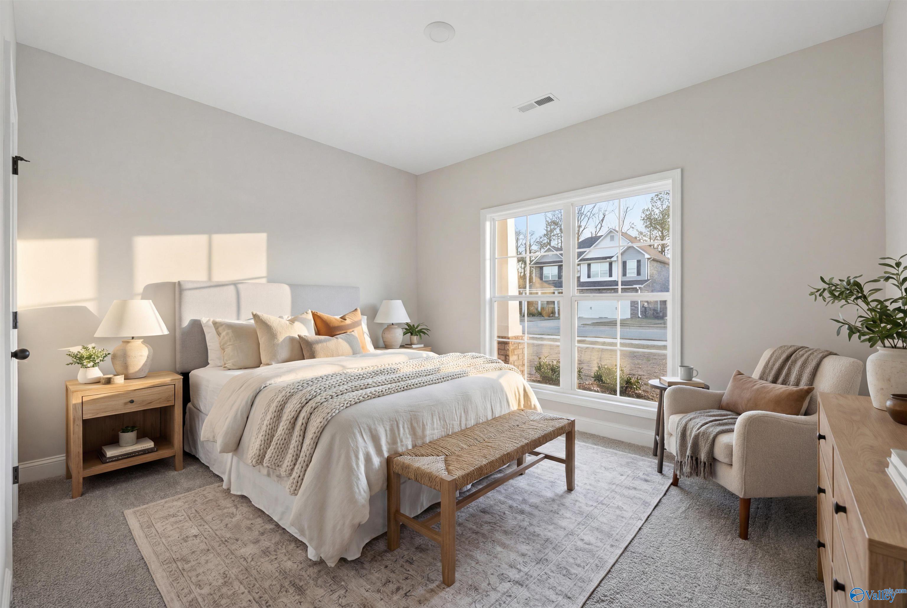 Cozy bedroom with neutral bedding, orange pillows, armchair, plants, and large window in Davidson Homes The Daphne D, Arab, Alabama