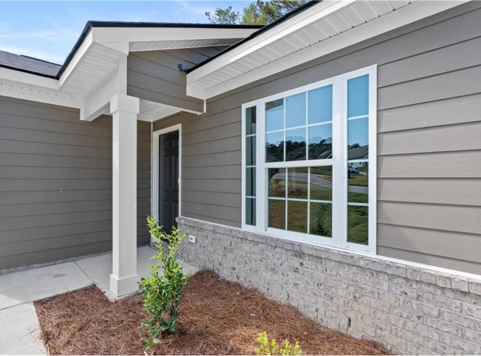 Gray-sided single-story home with large white-framed window, black front door, brick base, and porch columns in Phenix City, Alabama