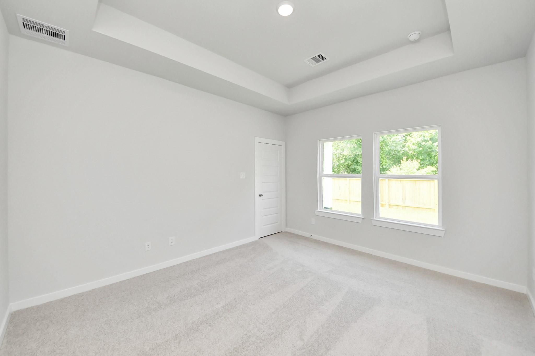 Bright bedroom with tray ceiling and plush carpet in The Blanco E floor plan at Caney Creek Place, Conroe, Texas.