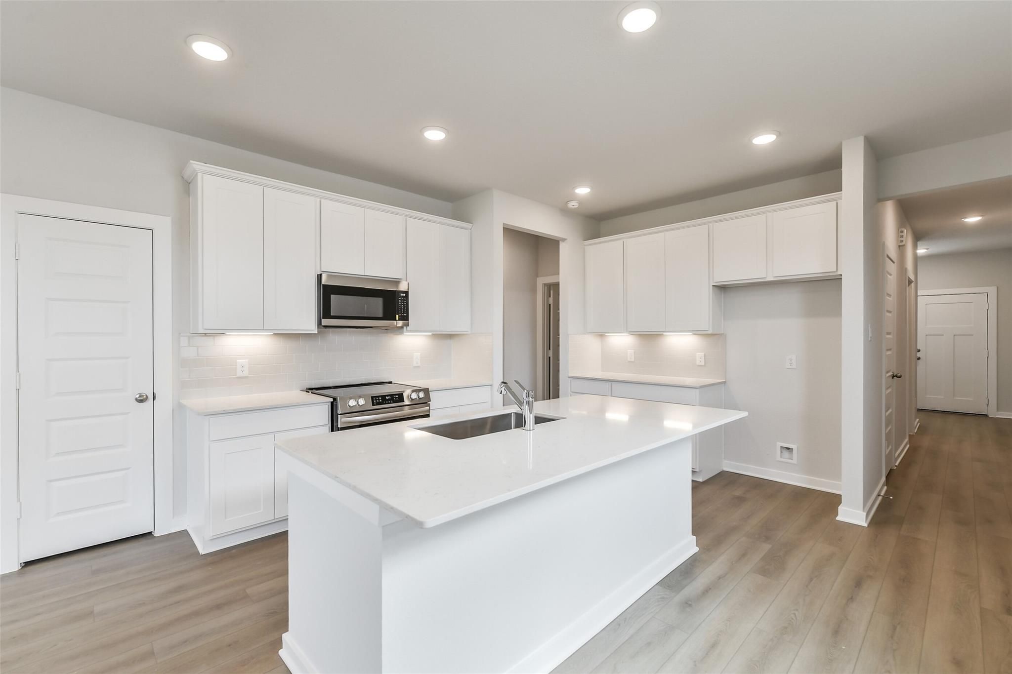 Bright modern kitchen with white quartz island, stainless appliances, and recessed lighting in Davidson Homes The Frio G, Cleveland TX