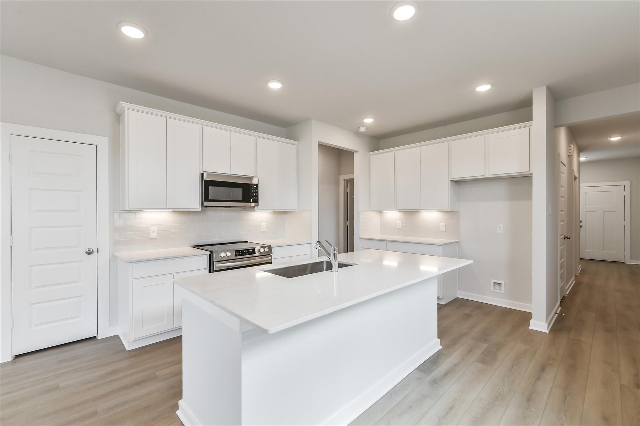 Bright modern kitchen with white quartz island, stainless appliances, and recessed lighting in Davidson Homes The Frio G, Cleveland TX