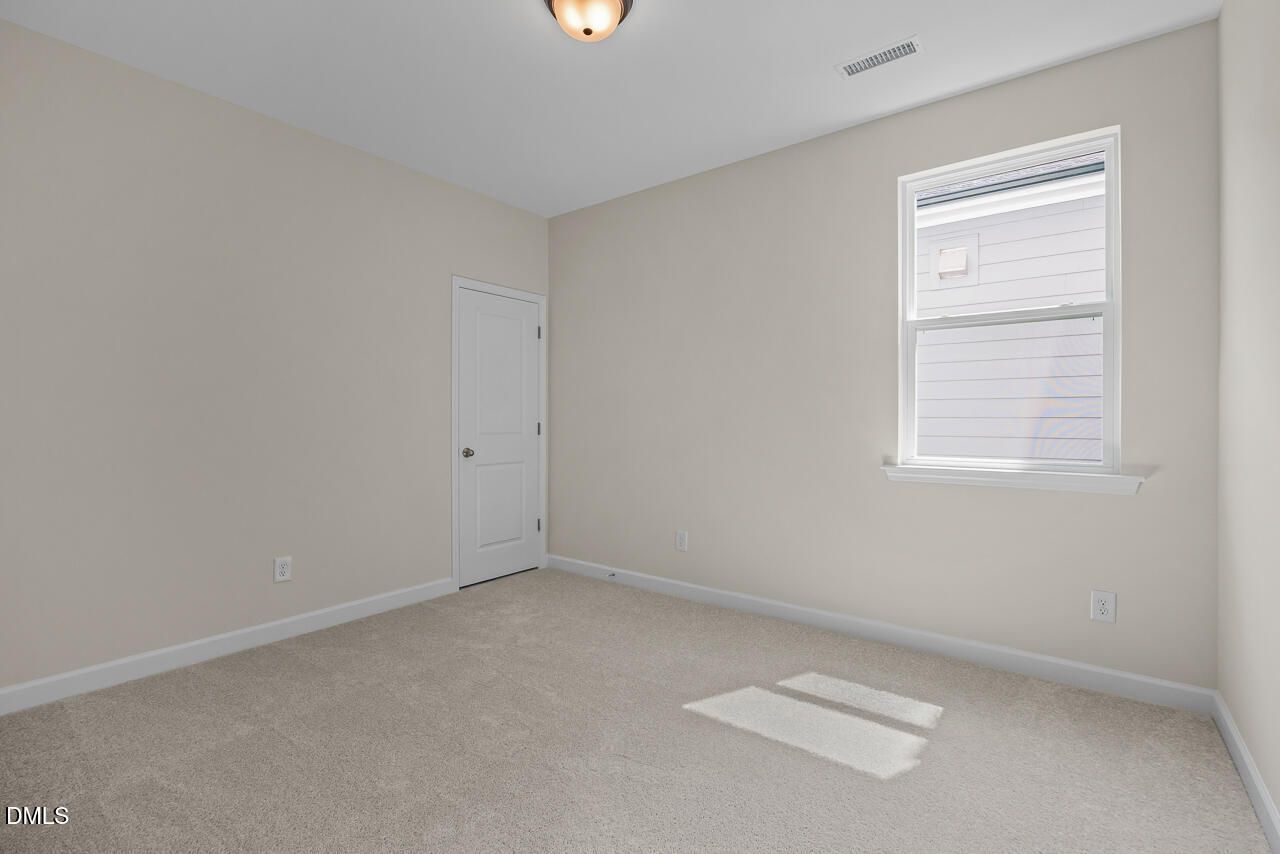 Bright empty bedroom with carpet, white door, and window in Davidson Homes The Birch II C, Sage on North Main, Wake Forest, NC