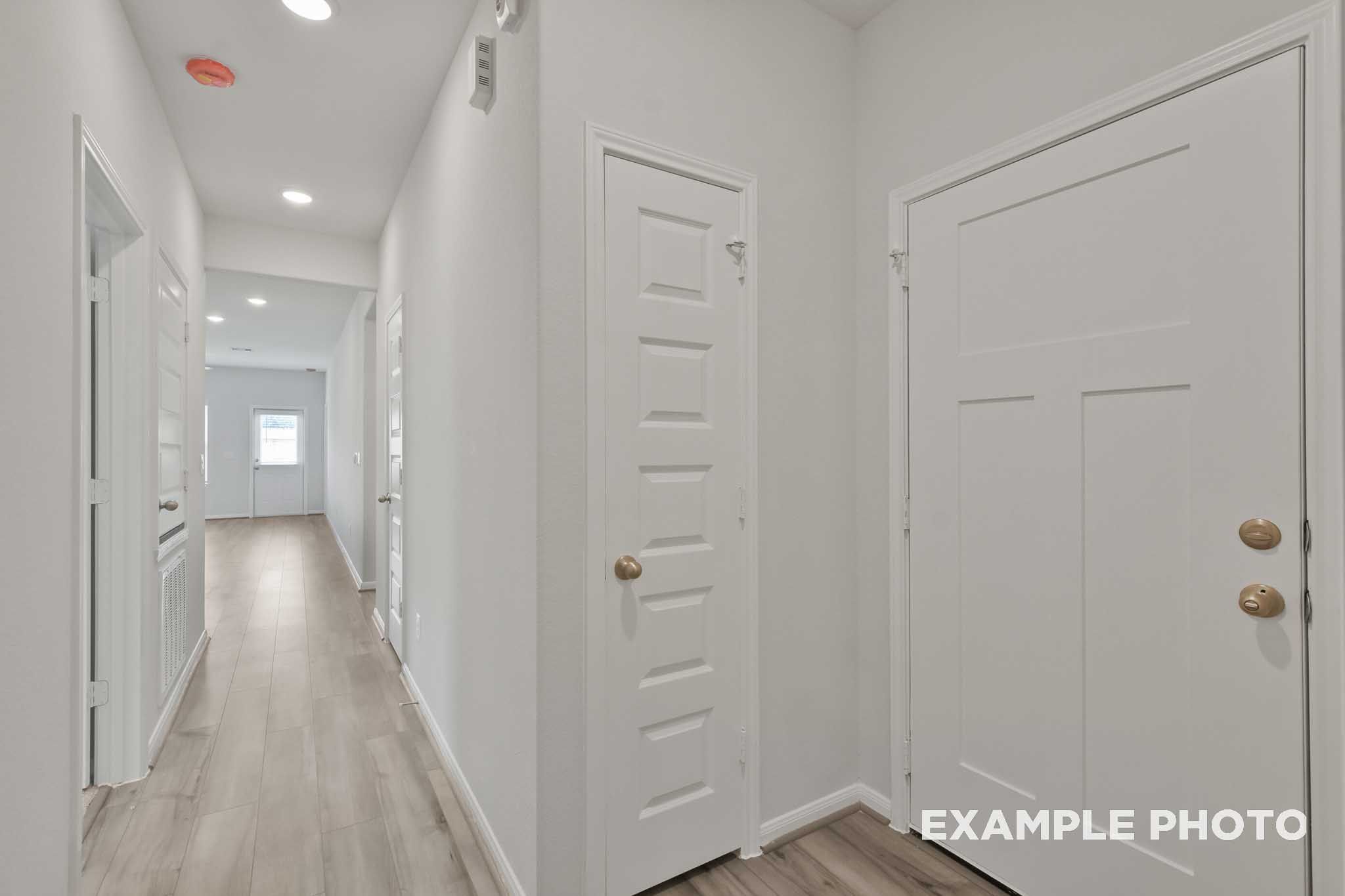Spacious hallway in The Comal home with light oak flooring, white walls, paneled doors, and recessed lighting
