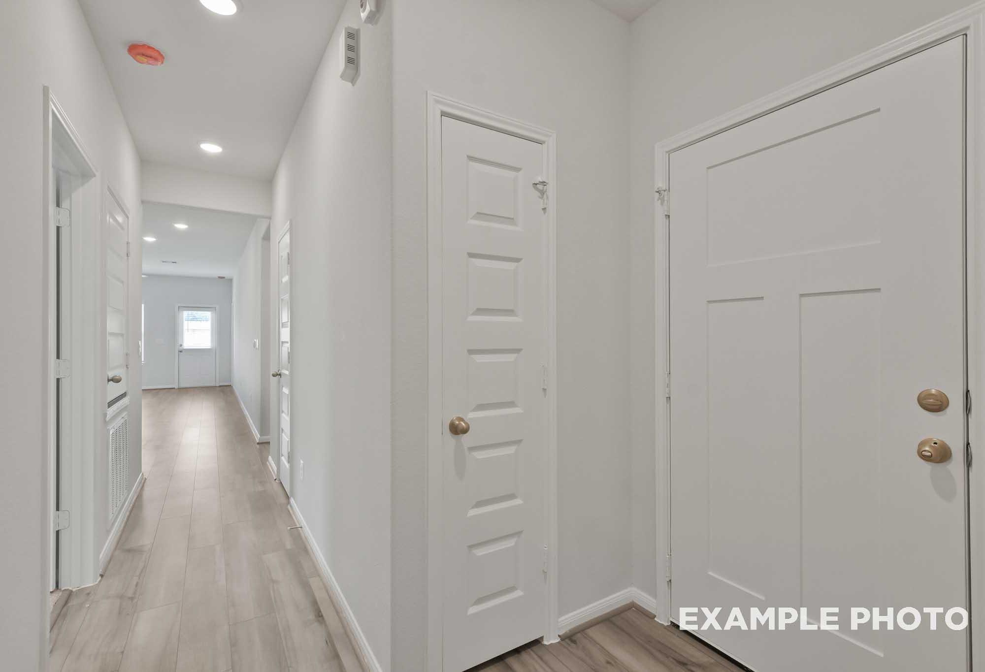 Spacious hallway in The Comal home with light oak flooring, white walls, paneled doors, and recessed lighting