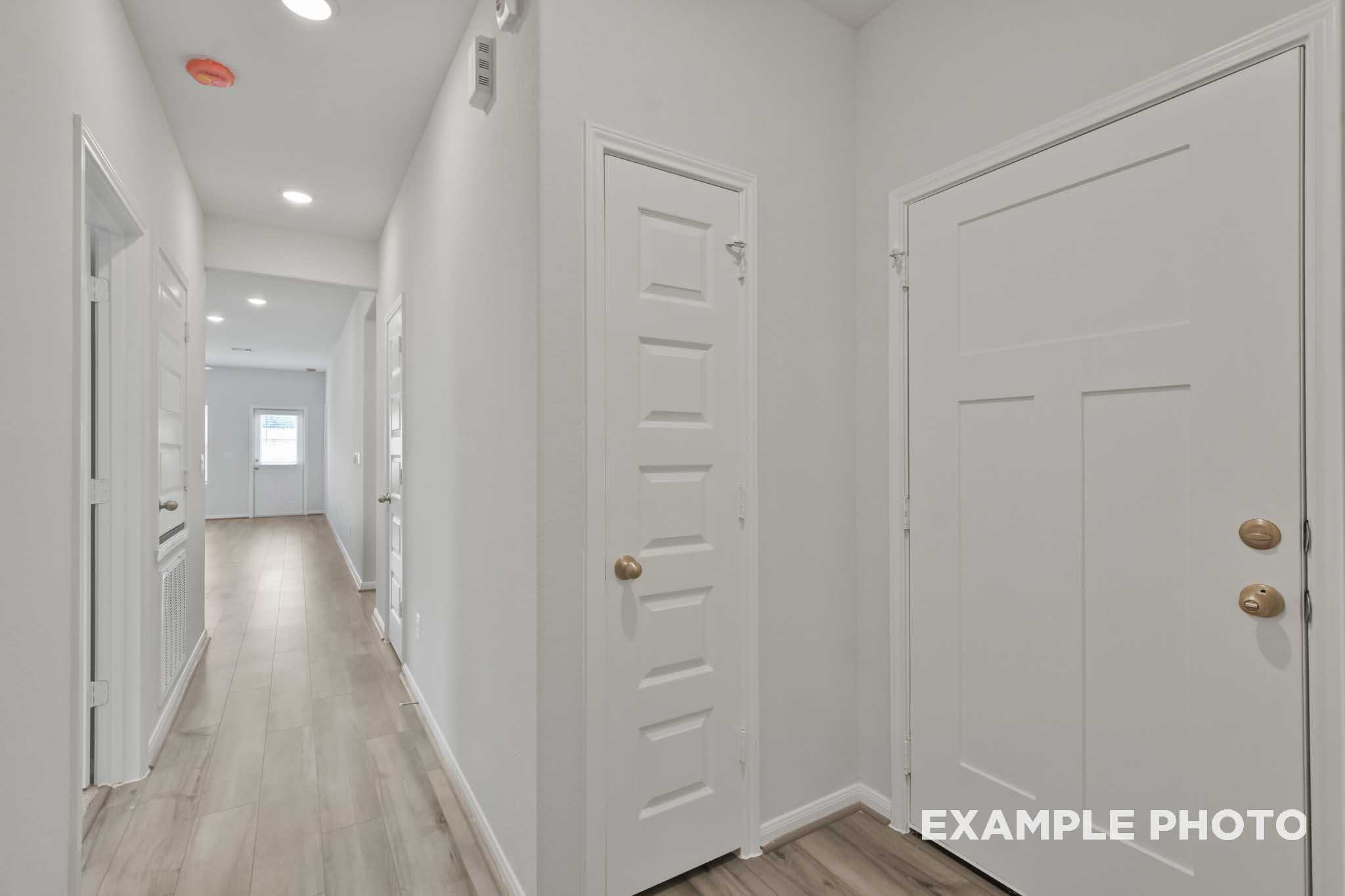 Spacious hallway in The Comal home with light oak flooring, white walls, paneled doors, and recessed lighting