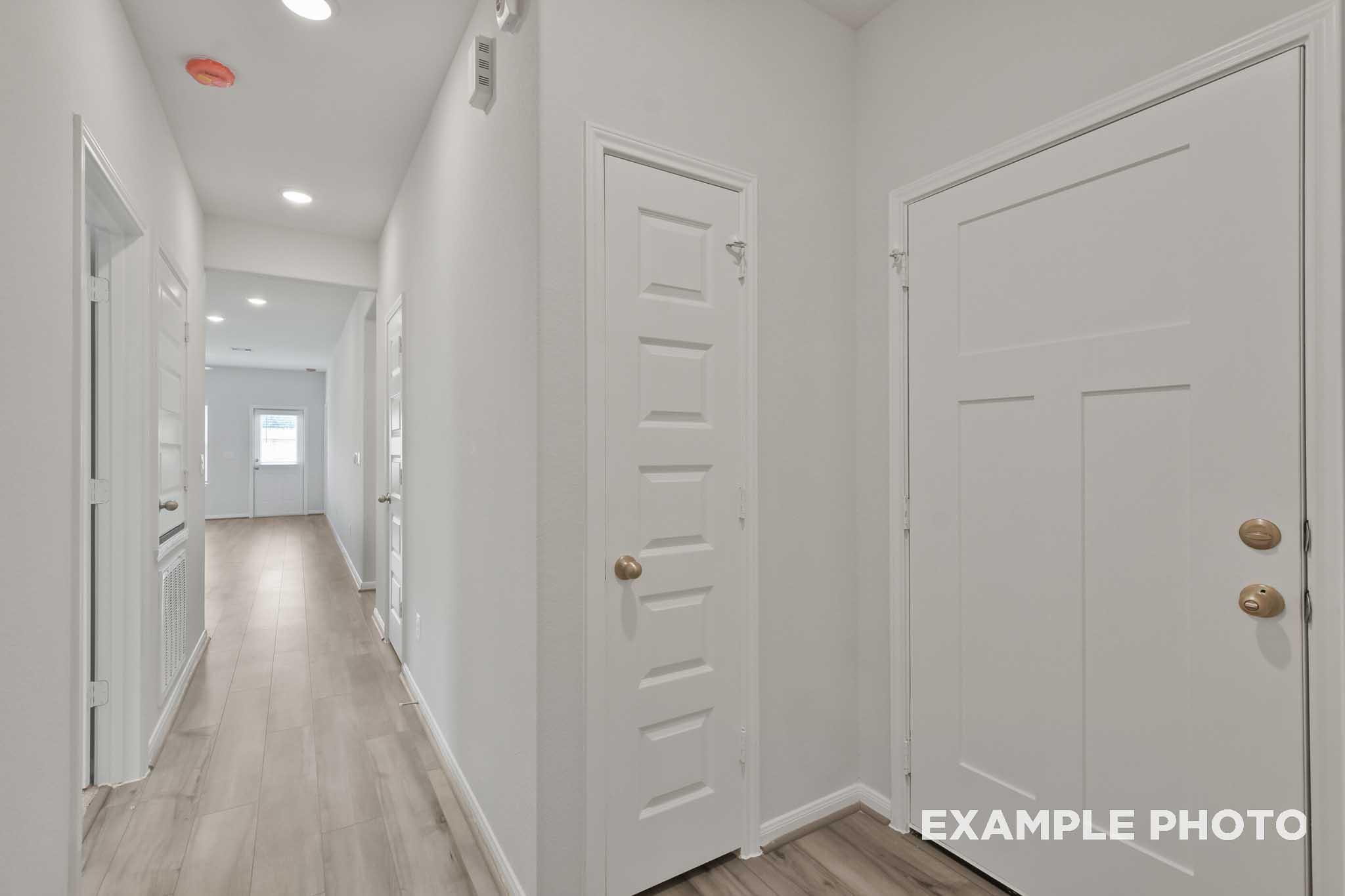 Spacious hallway in The Comal home with light oak flooring, white walls, paneled doors, and recessed lighting