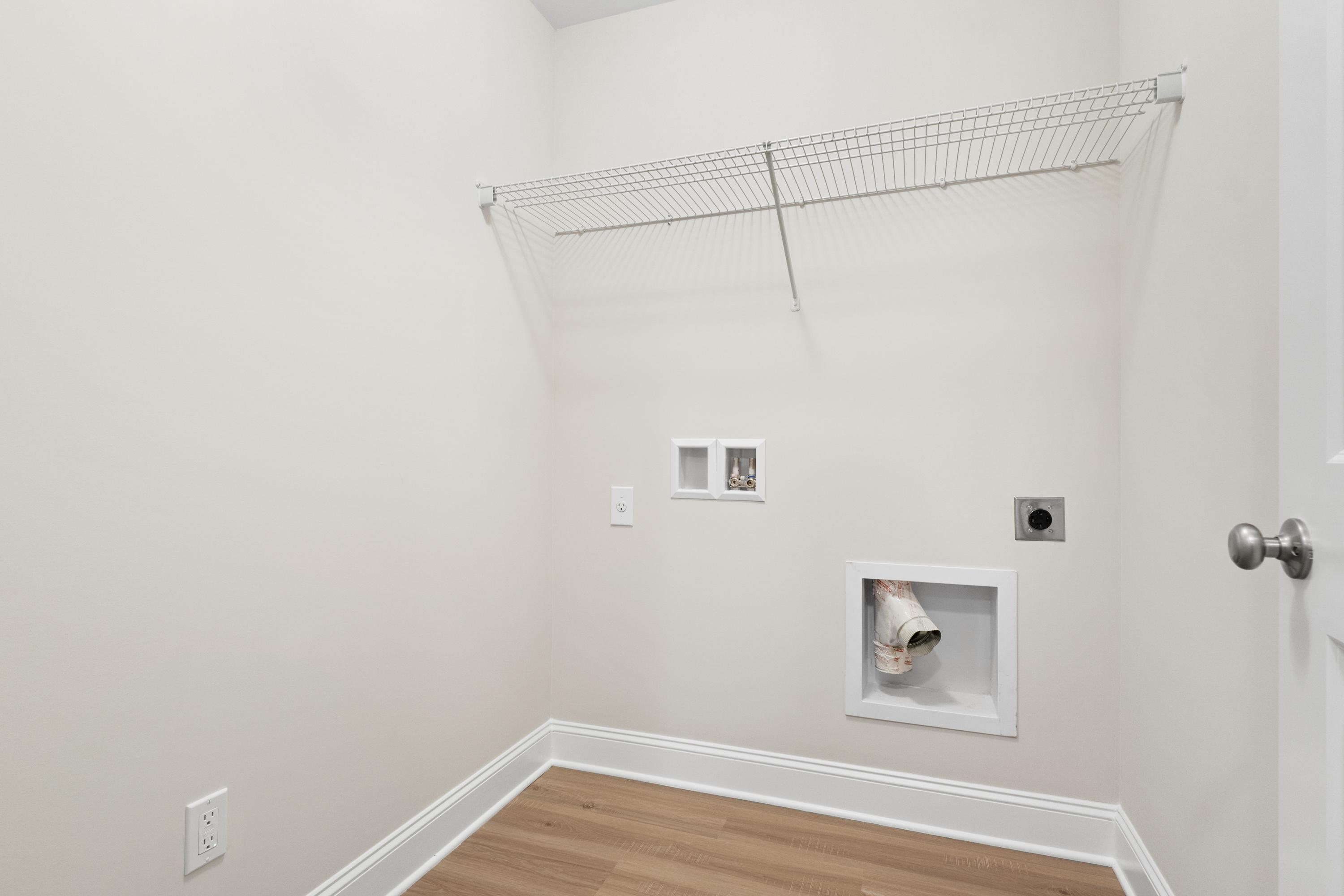 Spacious laundry room in The Asheville home with wire shelving, washer dryer hookups, neutral walls, hardwood floors