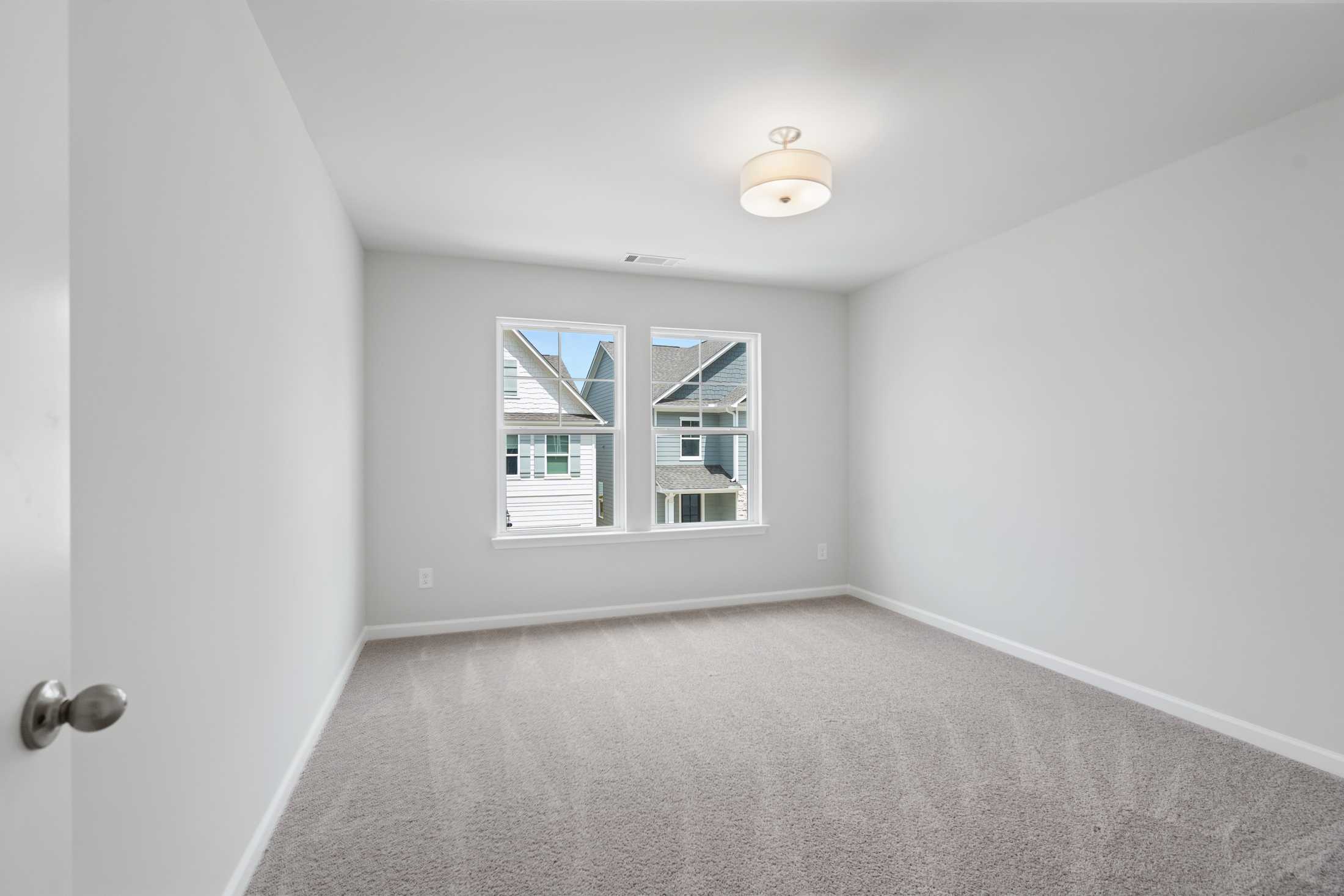 Spacious upstairs bedroom in The Cary A design with light gray walls, beige carpet, large windows overlooking neighborhood, ceiling light