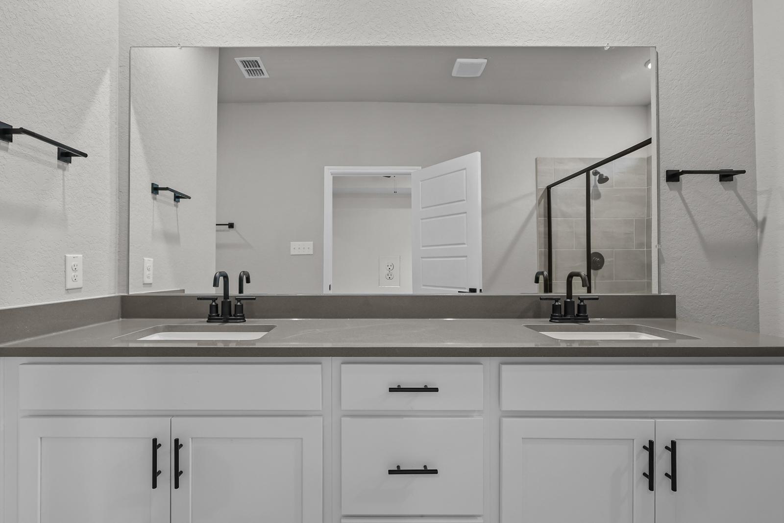 Modern master bathroom in The Glenwood featuring a double vanity with white cabinets, dark hardware, and quartz countertop.
