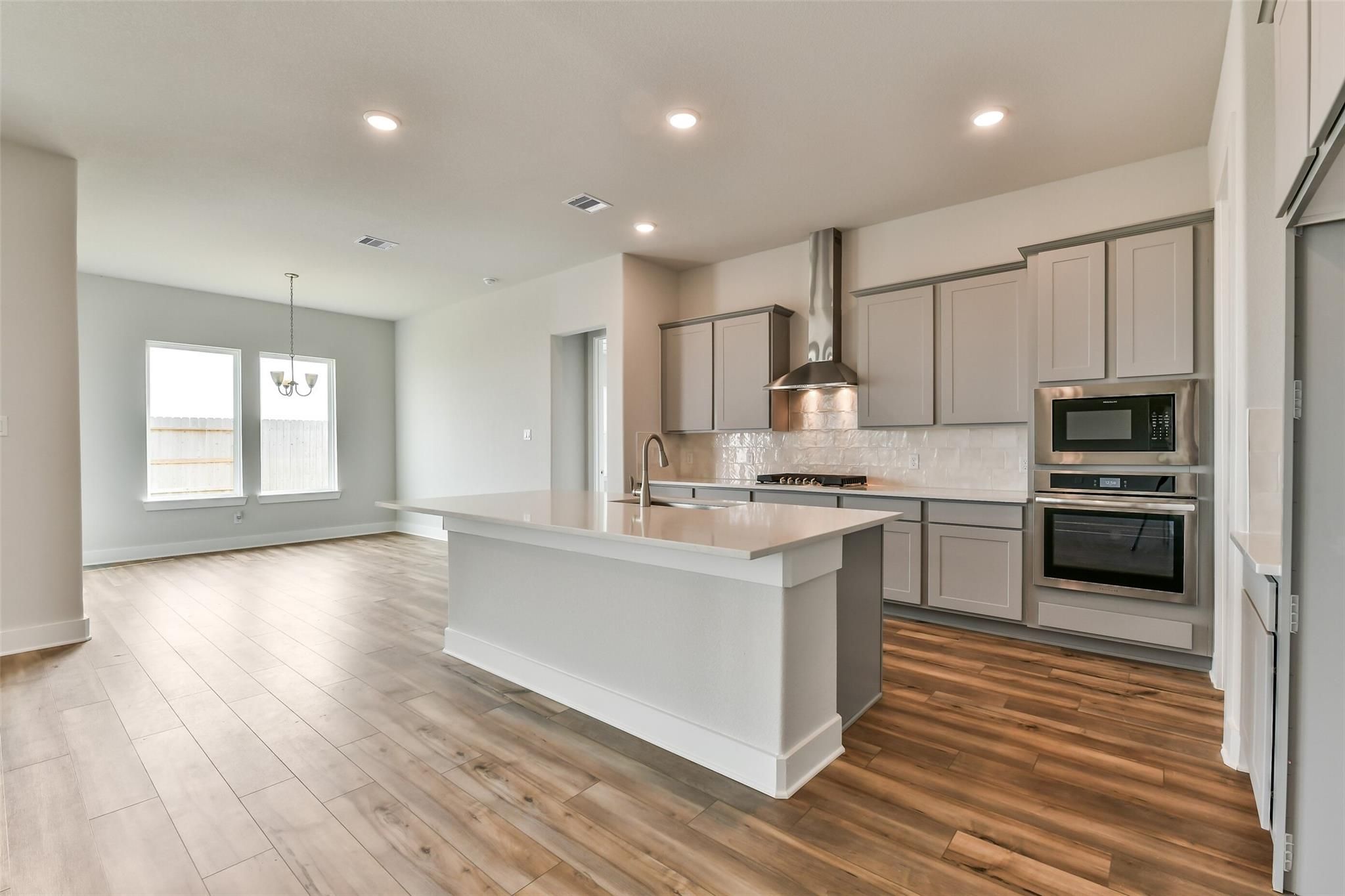 Modern open-concept kitchen with gray shaker cabinets, stainless steel appliances, white island, and hardwood floors in Davidson Homes The George A, Lago Mar