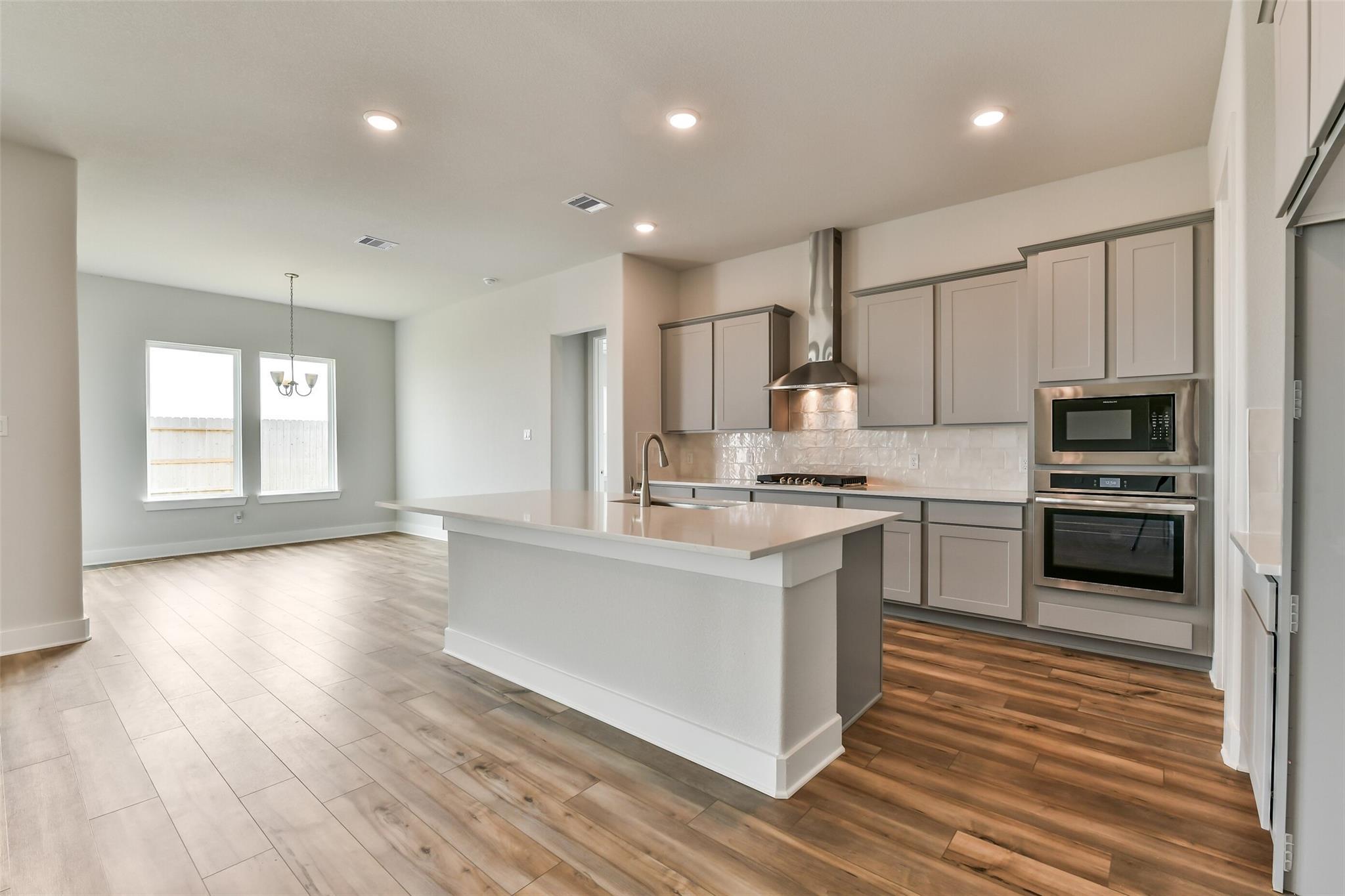 Modern open-concept kitchen with gray shaker cabinets, stainless steel appliances, white island, and hardwood floors in Davidson Homes The George A, Lago Mar