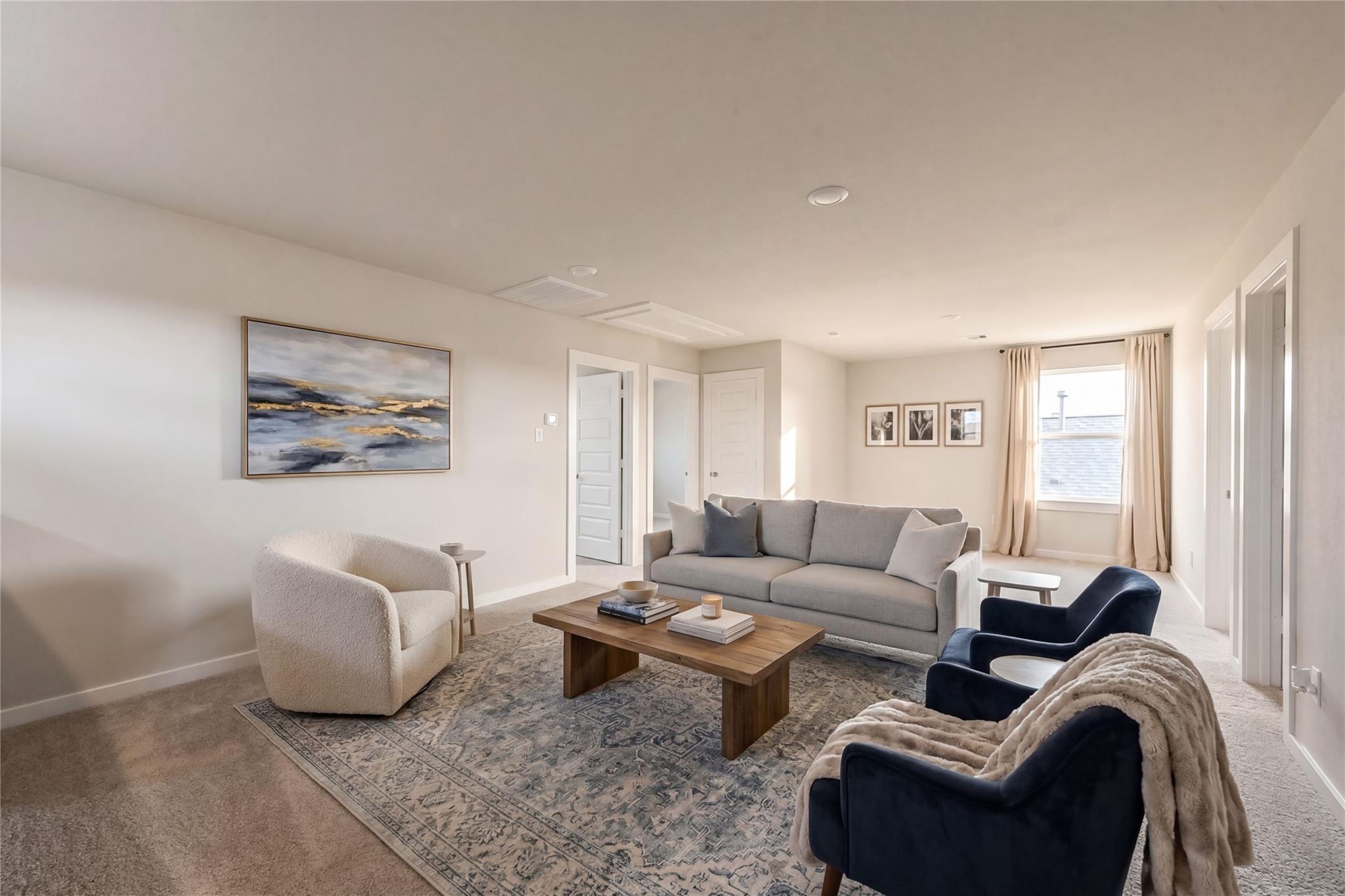Cozy living room with gray sectional sofa, cream armchair, blue velvet chairs, wooden coffee table, and abstract art in Davidson Homes The Brazos E, Dayton, Texas