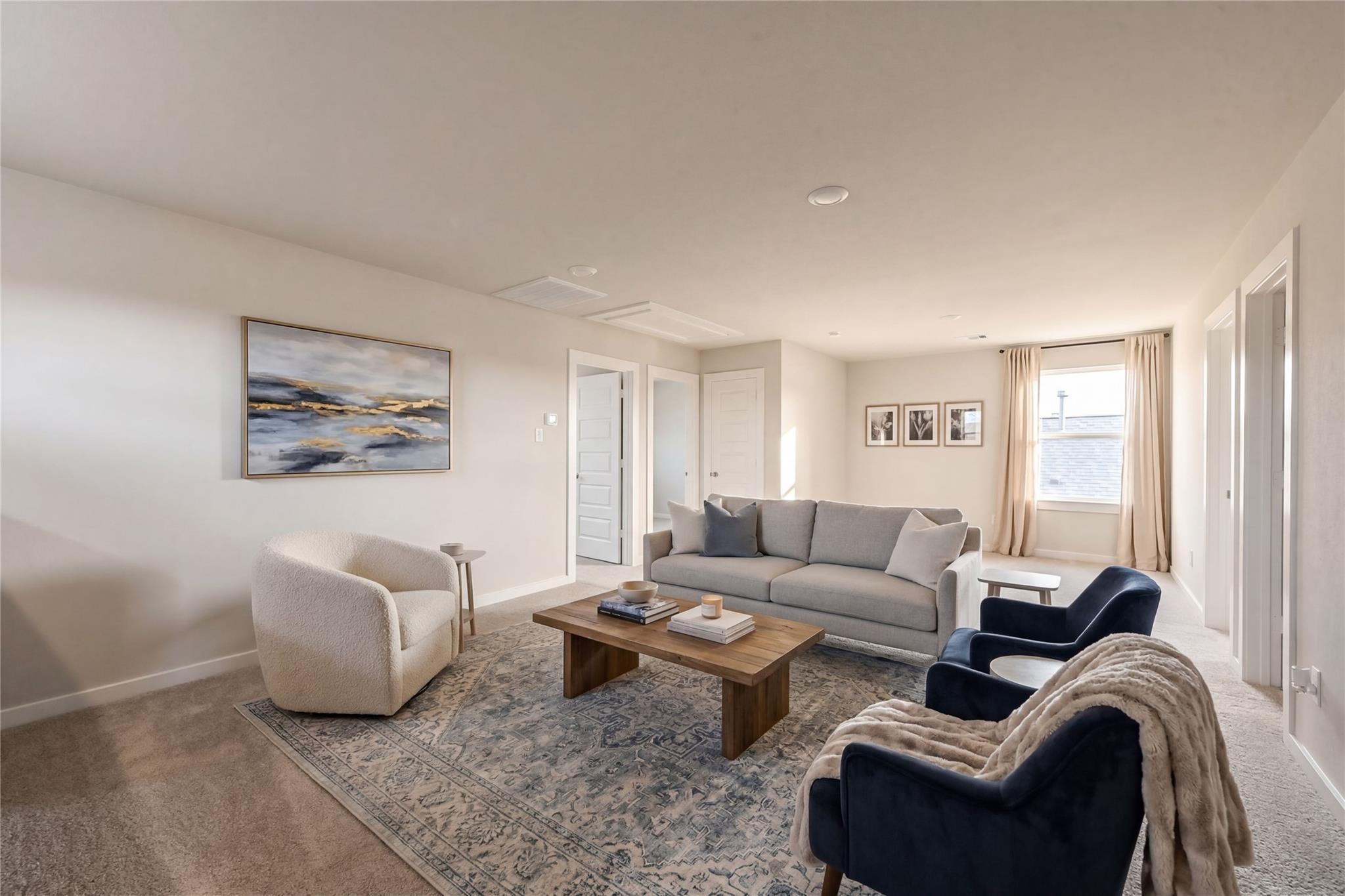 Cozy living room with gray sectional sofa, cream armchair, blue velvet chairs, wooden coffee table, and abstract art in Davidson Homes The Brazos E, Dayton, Texas