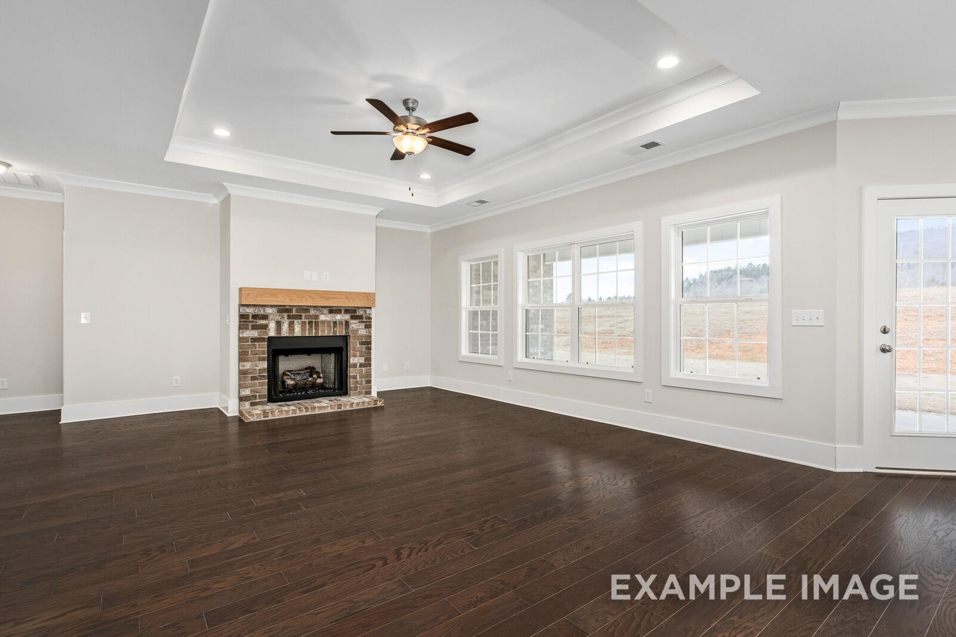 Spacious living room in The Rockford home design featuring brick fireplace, hardwood floors, ceiling fan, and large windows