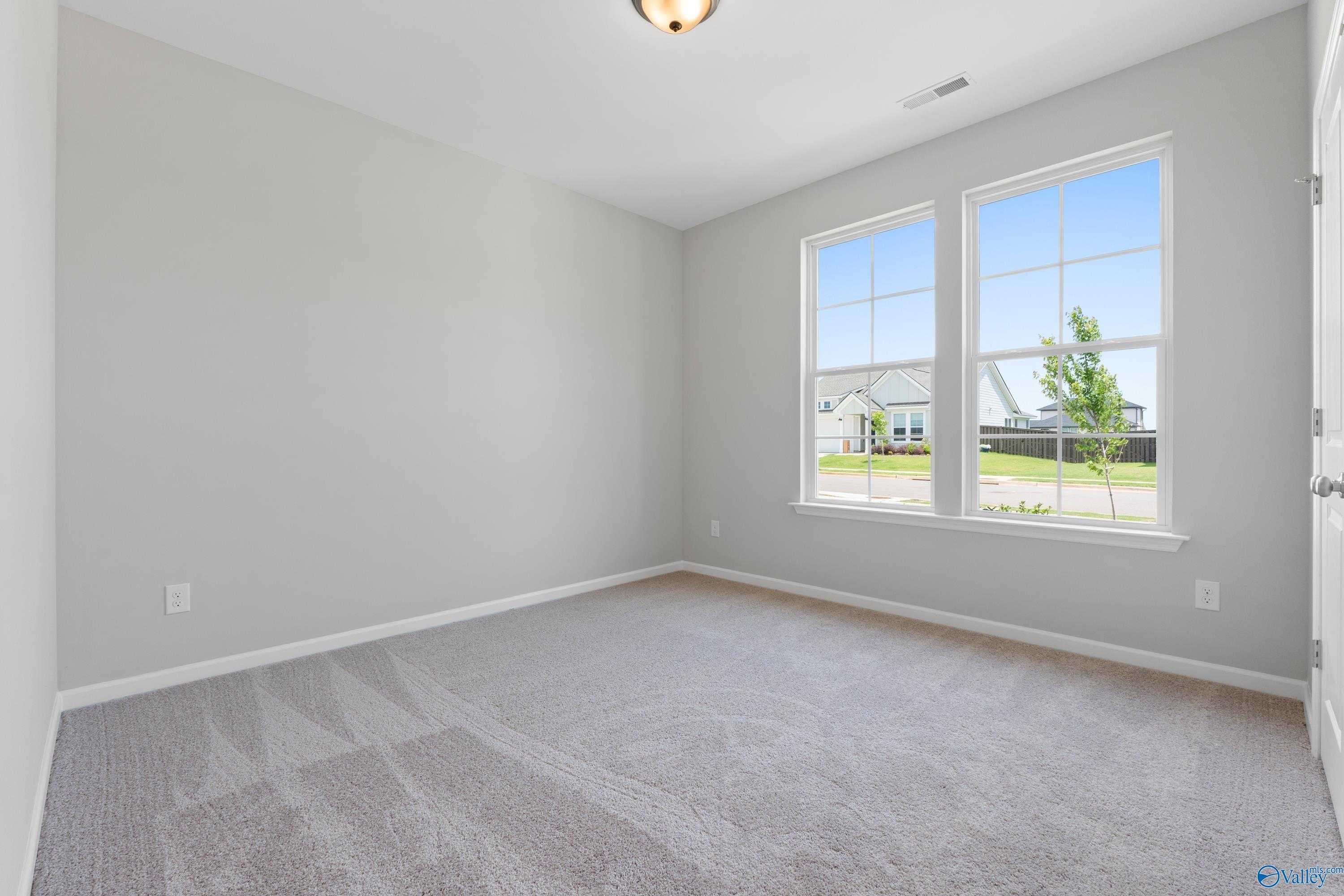 Bright secondary bedroom with gray walls, beige carpet, and large windows overlooking yard in Davidson Homes The Orion, Athens AL