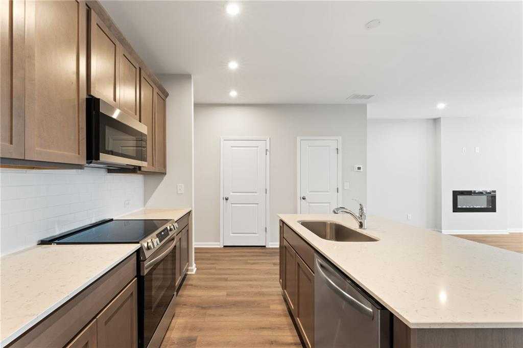 Modern kitchen with warm wood shaker cabinets, quartz island sink, stainless appliances, subway tile backsplash in The Monroe A, Emerson GA