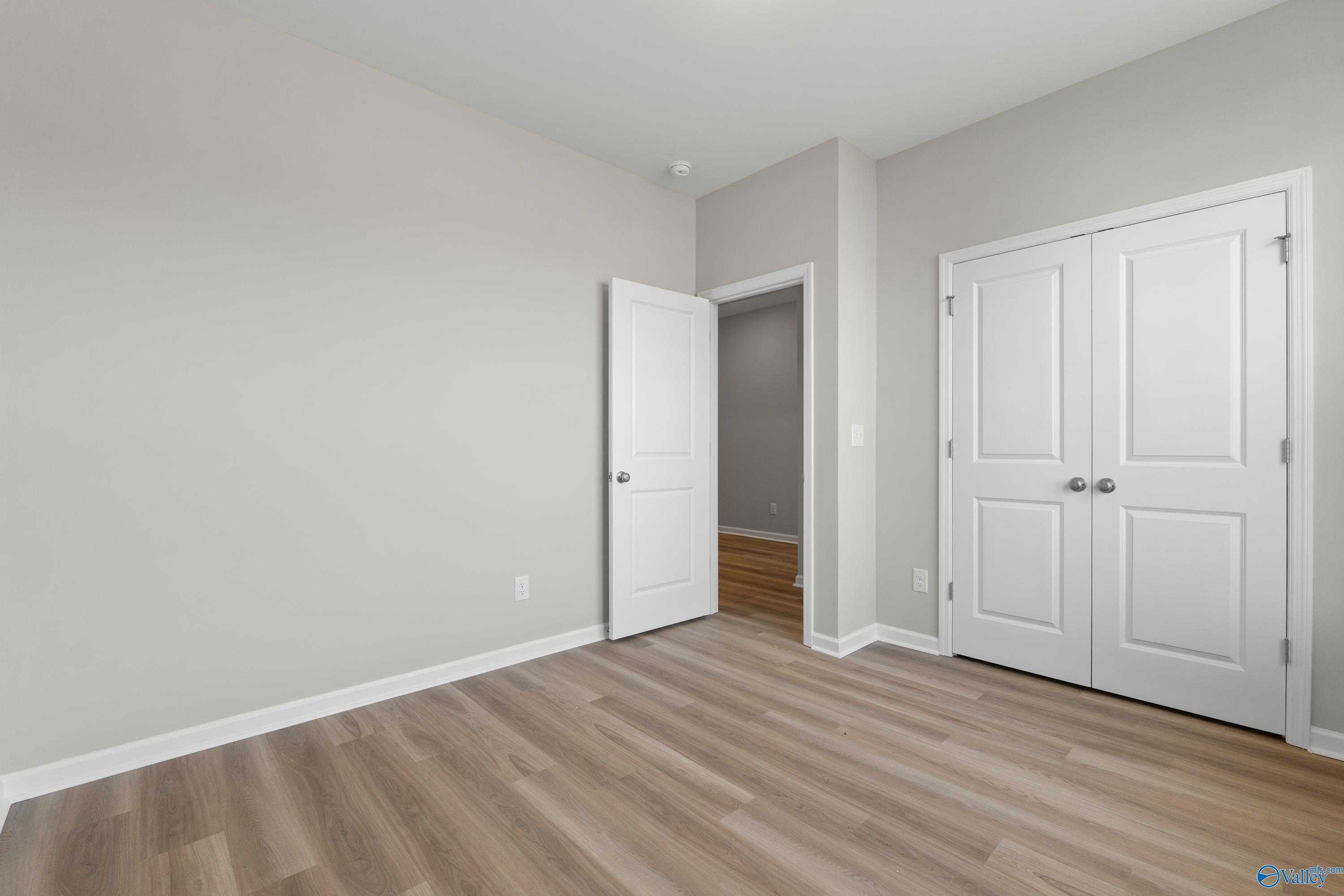 Spacious bedroom with light gray walls, white double closet doors, open entry, and luxury vinyl plank flooring in Davidson Homes The Polaris, Fayetteville, TN