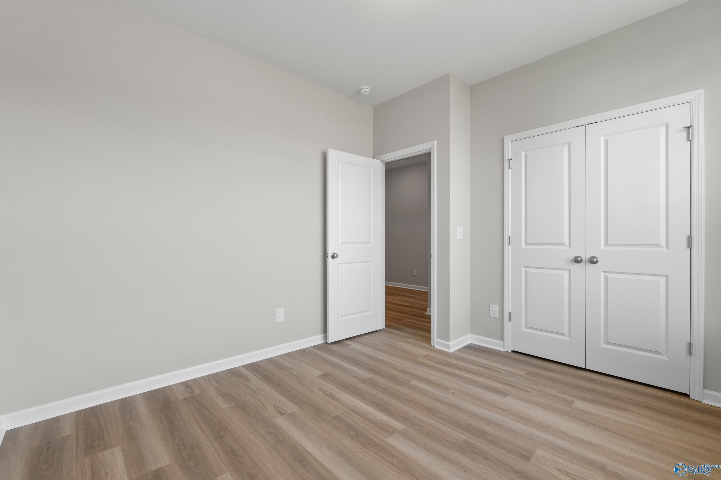 Bright bedroom with double-door closet, open entry to adjacent room, and light wood flooring in Davidson Homes The Polaris, Fayetteville, TN