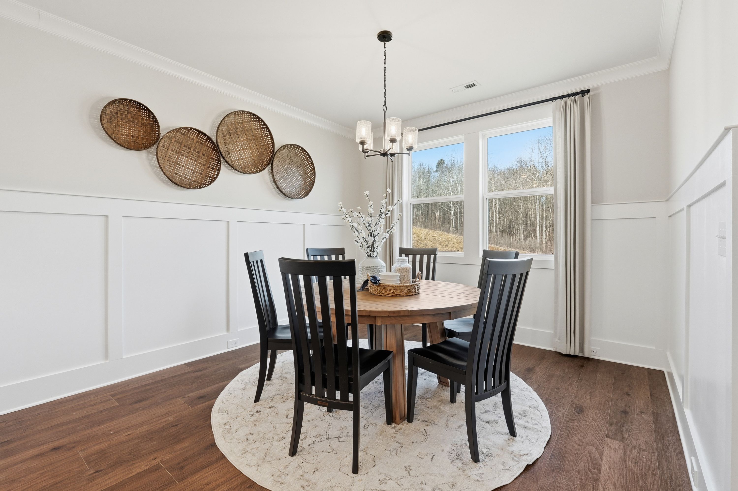 Spacious dining room at Noble Ridge in Cullman AL with round wooden table, black chairs, woven basket wall decor, chandelier, and large windows