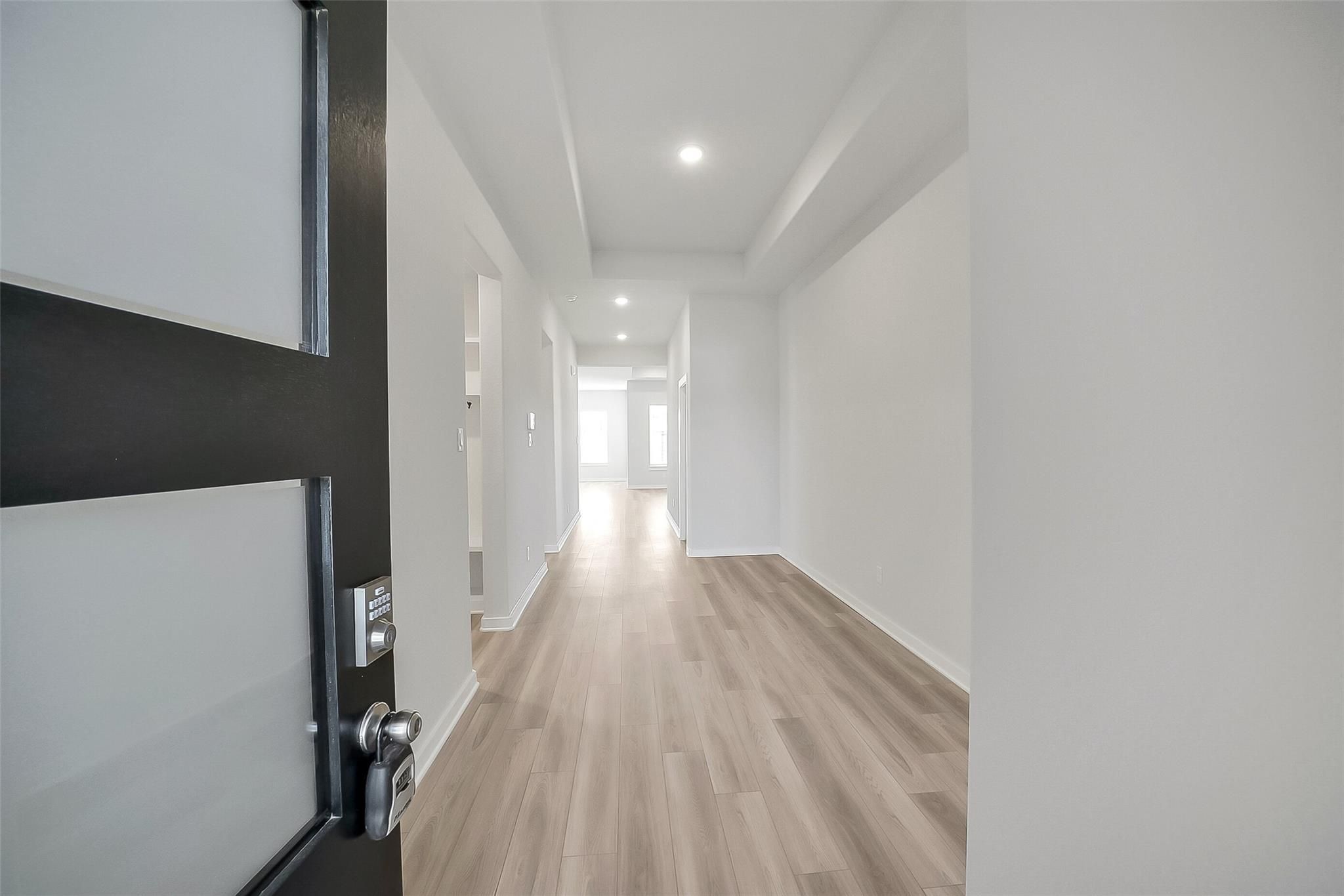 Modern entryway with black front door, frosted glass panel, and light oak floors in Davidson Homes The Acadia A, Katy, Texas