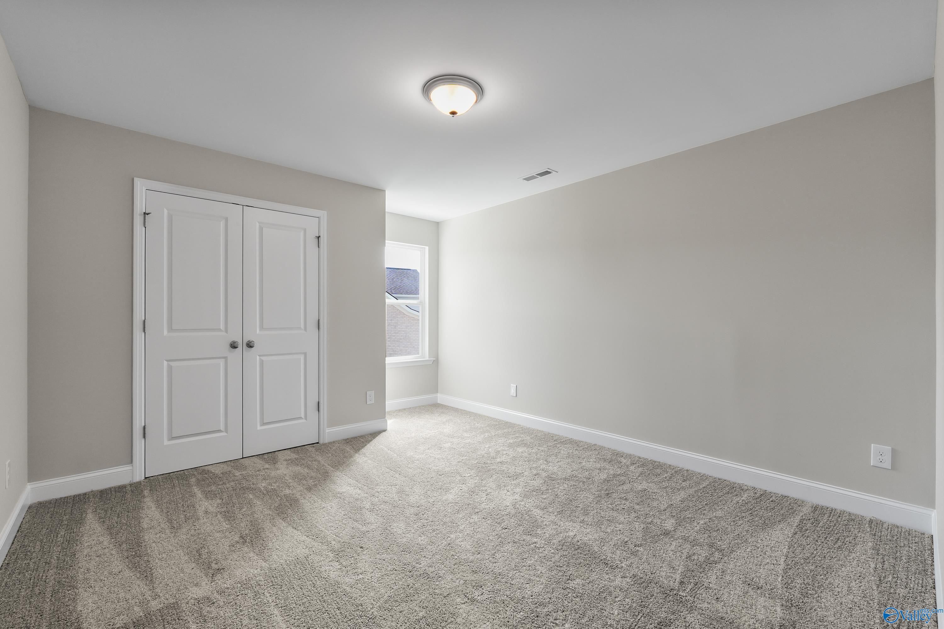 Empty bedroom with light gray walls, white double closet doors, carpet flooring, and side window in Evermore Homes The Haven, Owens Cross Roads, Alabama