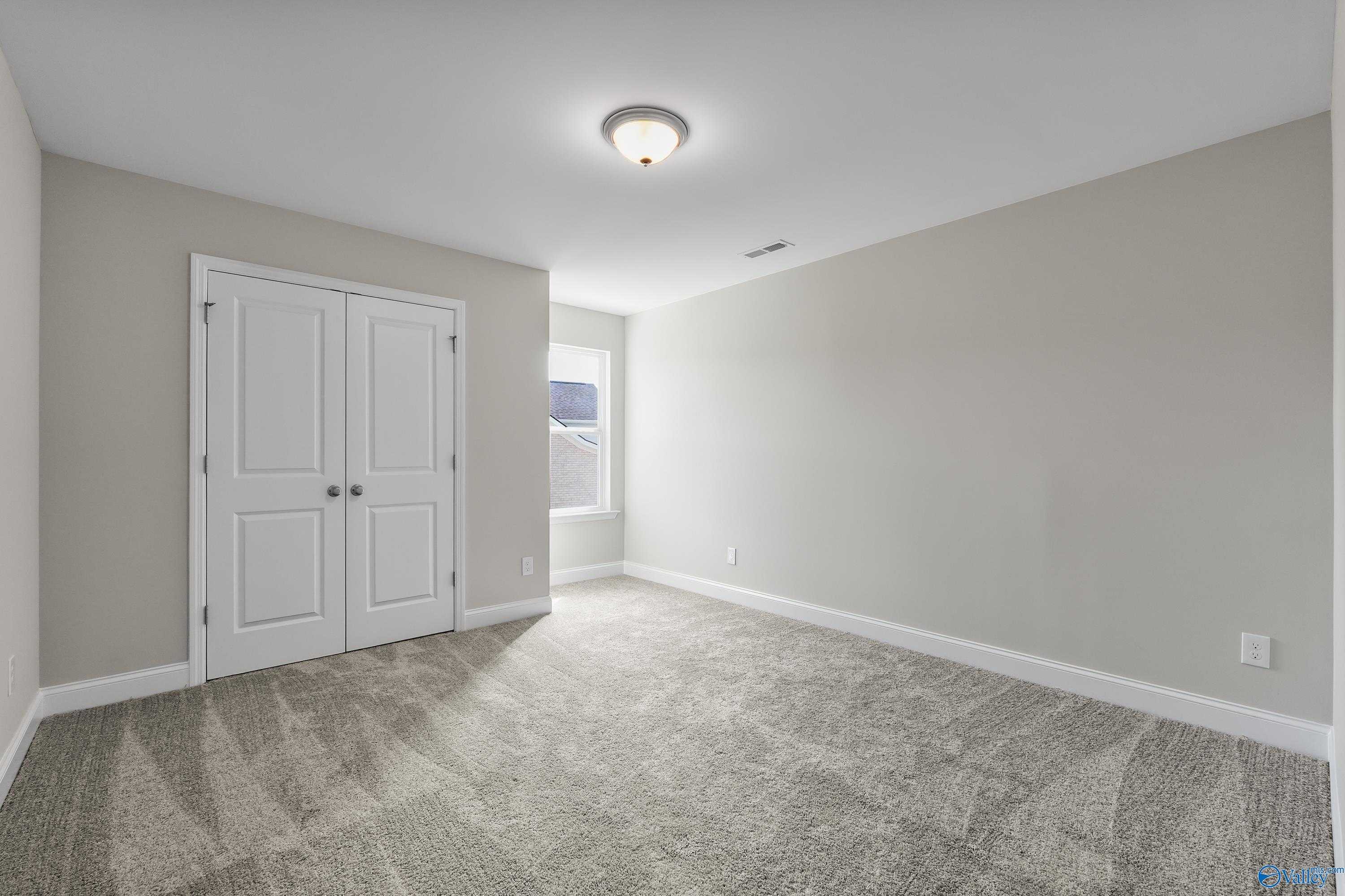Empty bedroom with light gray walls, white double closet doors, carpet flooring, and side window in Evermore Homes The Haven, Owens Cross Roads, Alabama