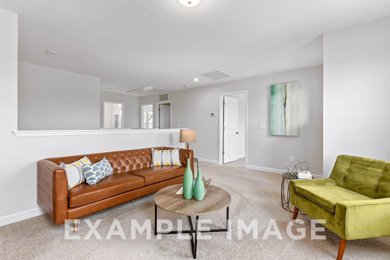 Cozy upstairs loft in The Willow C home design with brown leather sofa, green velvet chair, and wooden coffee table