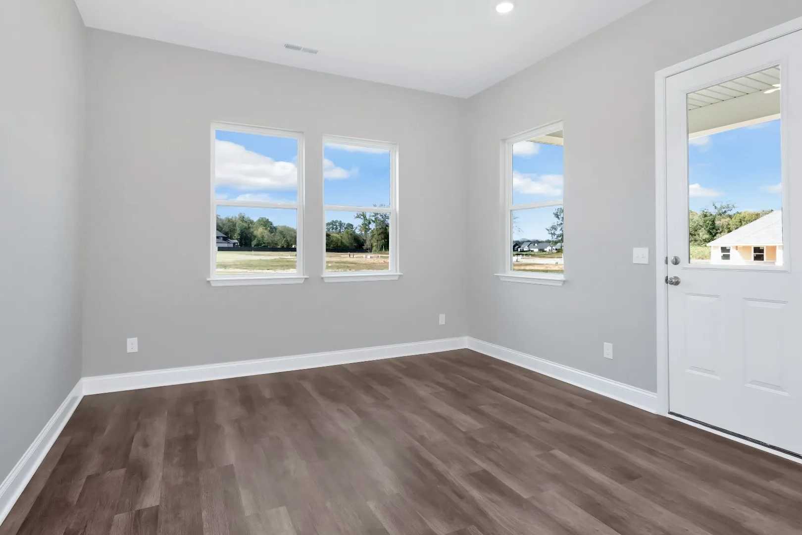 Spacious master bedroom in The Arcadia M by Evermore Homes with gray walls, large windows overlooking trees, hardwood floors
