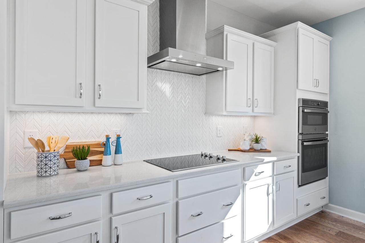 Modern kitchen in The Hemlock A featuring white cabinetry, chevron tile backsplash, stainless steel appliances, and island.
