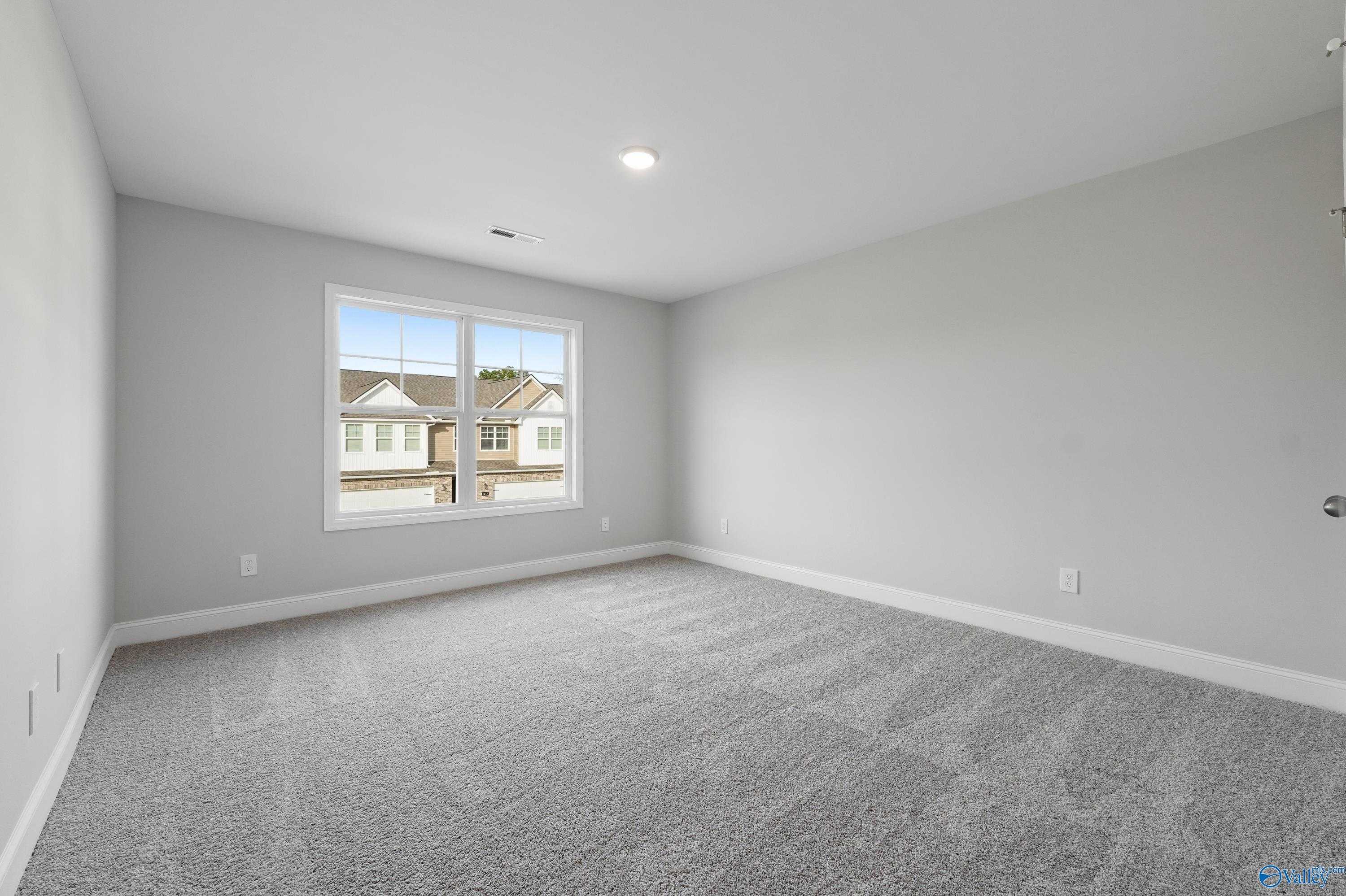 Empty secondary bedroom with gray carpet, light walls, and window view of neighborhood homes in Davidson Homes The Camden B, Huntsville, Alabama