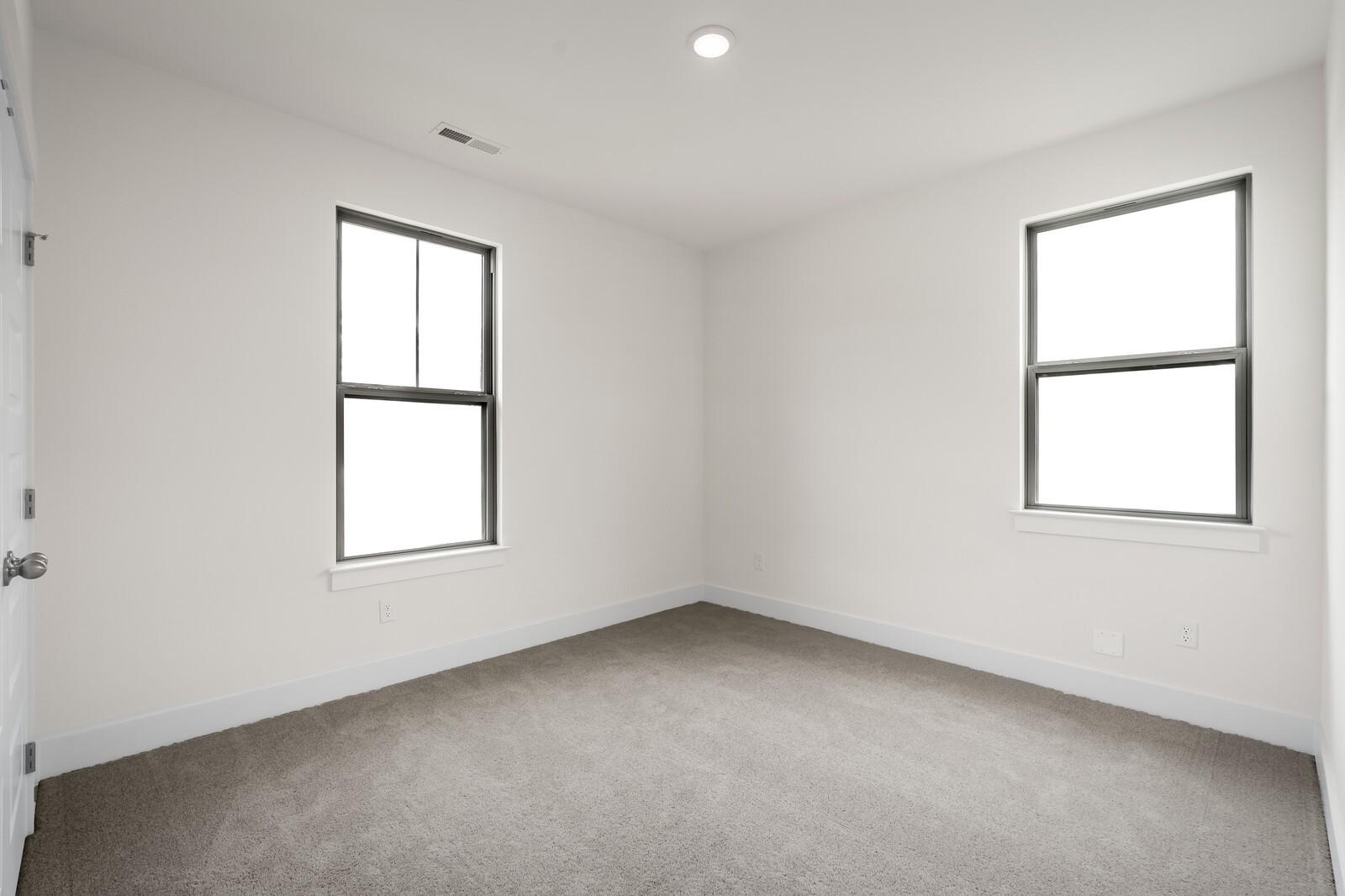 Bright, carpeted bedroom with neutral walls and windows in The Prairie C floor plan at Woods Crossing, Gallatin, TN.