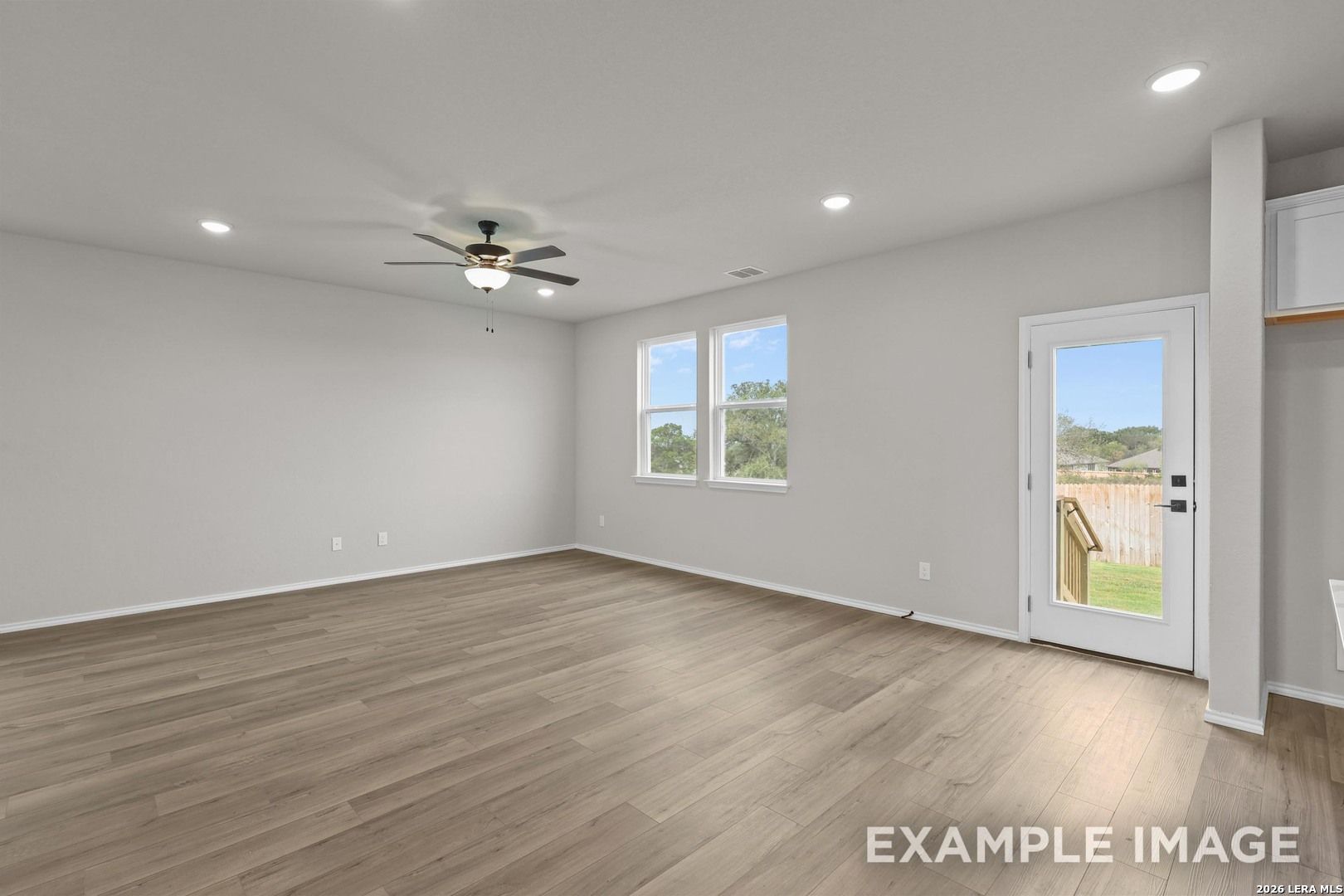 Bright living room with wood-look flooring, ceiling fan, and glass back door in Davidson Homes The Murray H, Converse, Texas