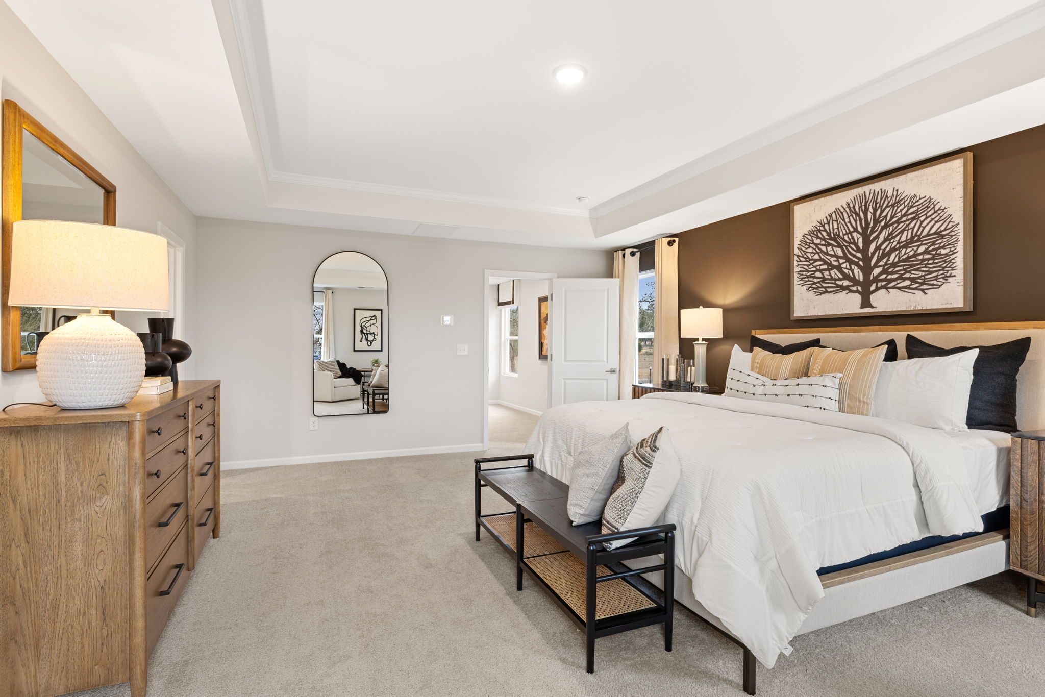 Spacious primary bedroom at Lake Shore in Winder GA featuring king bed, neutral tones, wooden dresser, and tree wall art