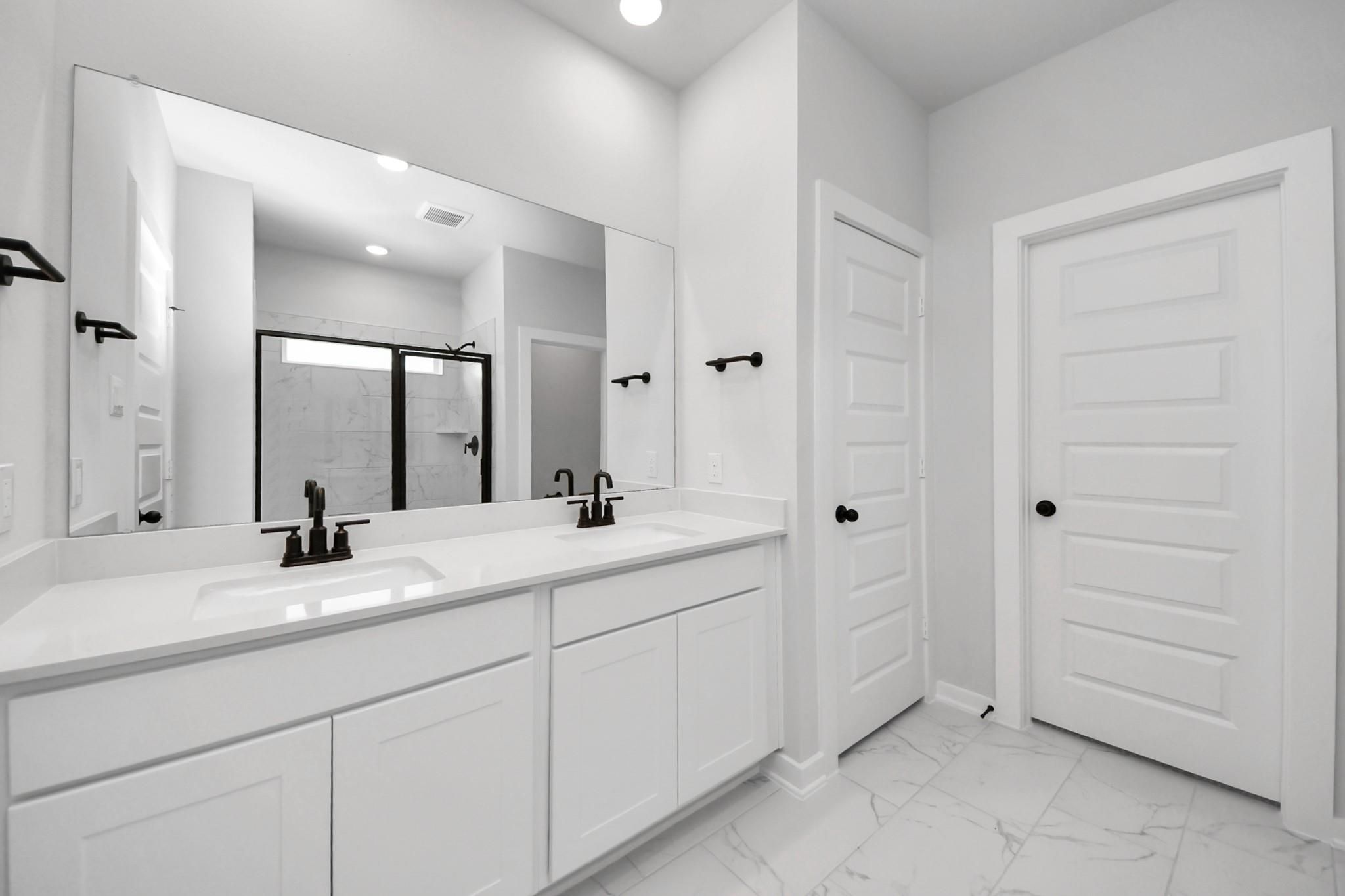 Modern primary bathroom with double vanity, white cabinets, and black fixtures in The Everett C home at River Ranch Meadows.