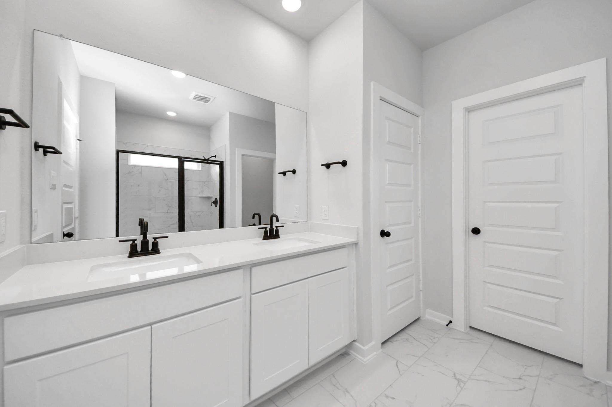 Modern primary bathroom with double vanity, white cabinets, and black fixtures in The Everett C home at River Ranch Meadows.
