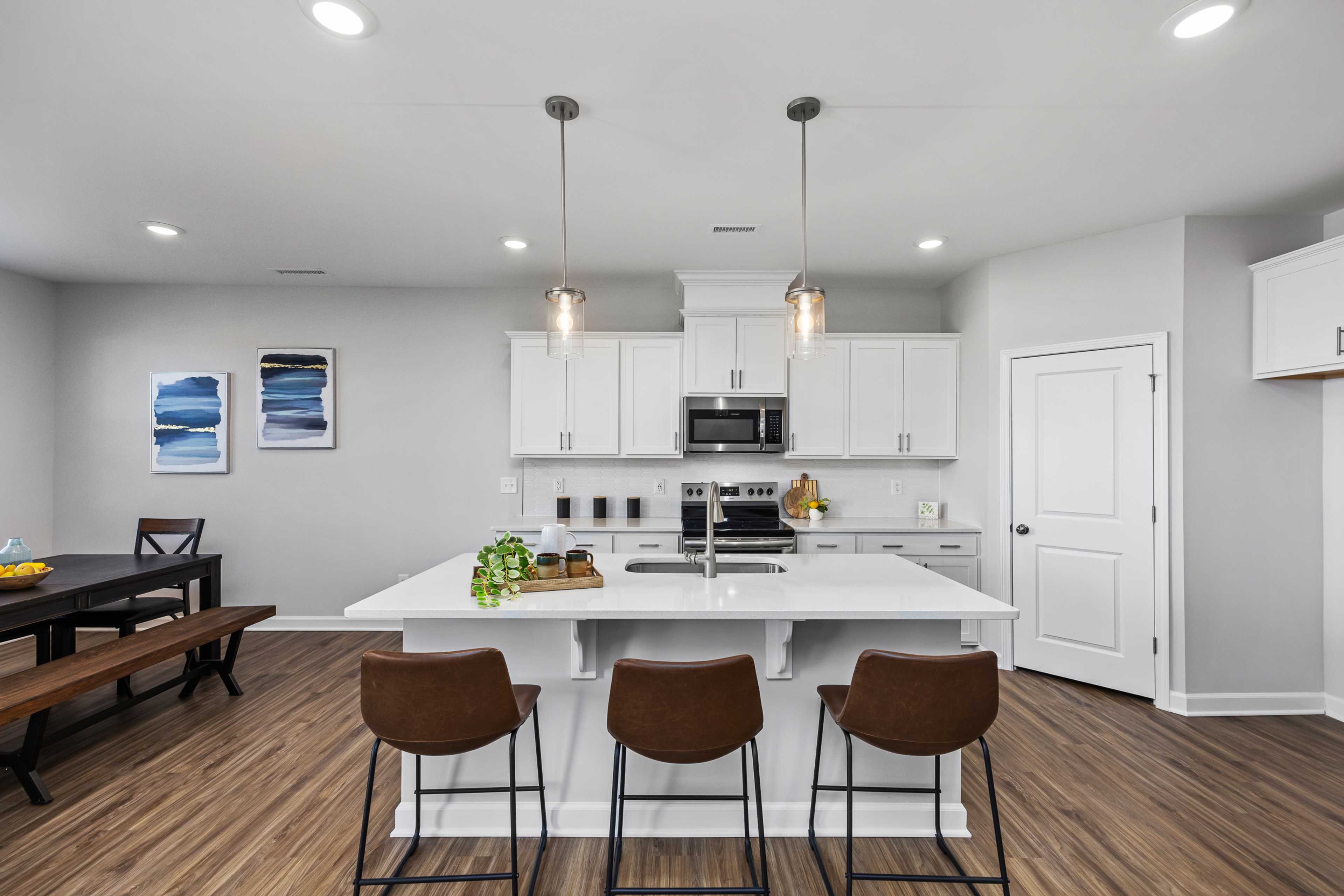 Modern kitchen with white cabinets, island bar stools, hardwood floors, and dining table at Woodland Crossing, Zebulon NC