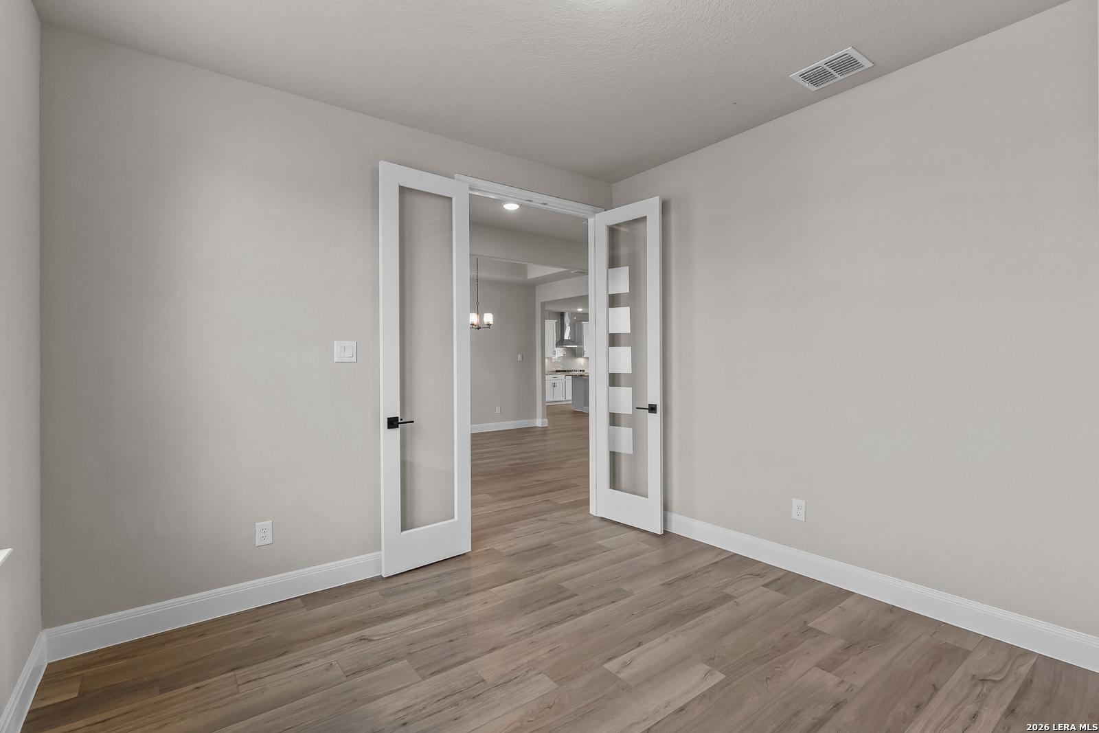 Flexible bedroom with glass-panel French doors and wood-look flooring in Davidson Homes The Foster E, Potranco Oaks, Castroville