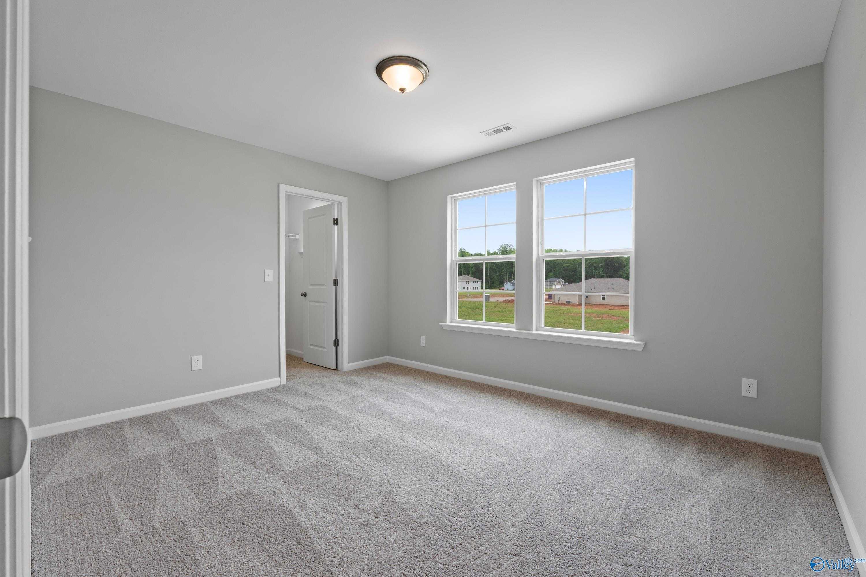 Spacious empty bedroom with gray carpet, light walls, ceiling fan, and large windows overlooking green field in The Stella home, Hazel Green, Alabama