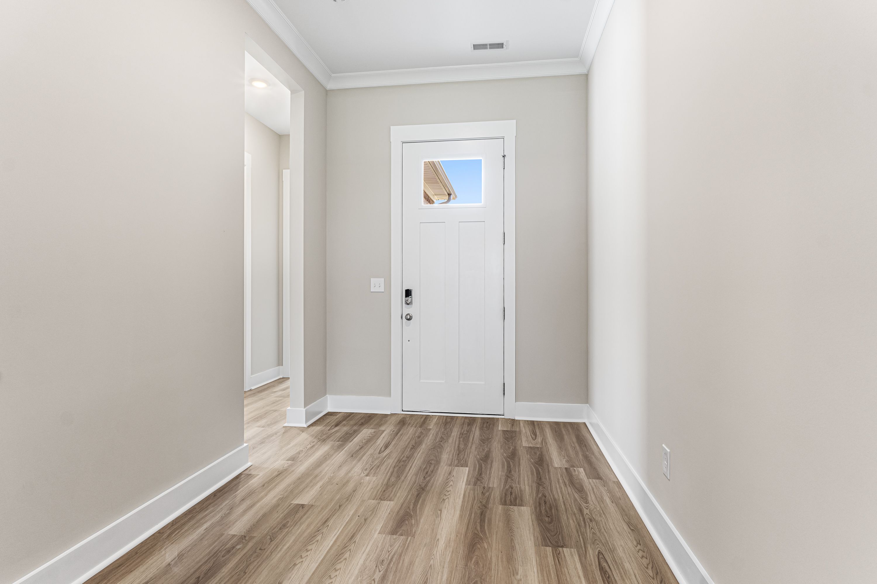 Spacious hallway in The Oxford A with beige walls, white paneled door, and light hardwood floors